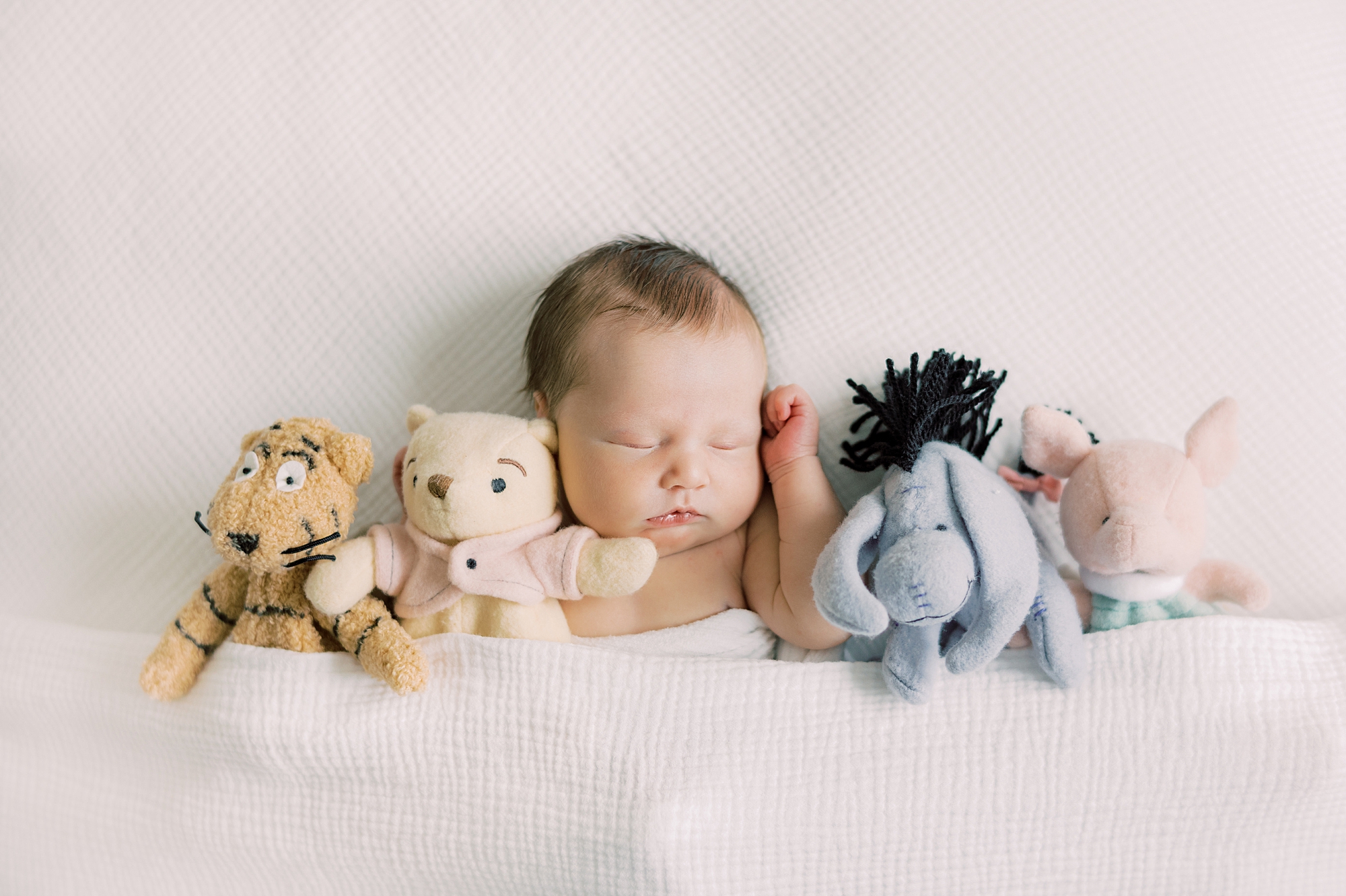 baby lays with Winnie the Pooh stuffed animals