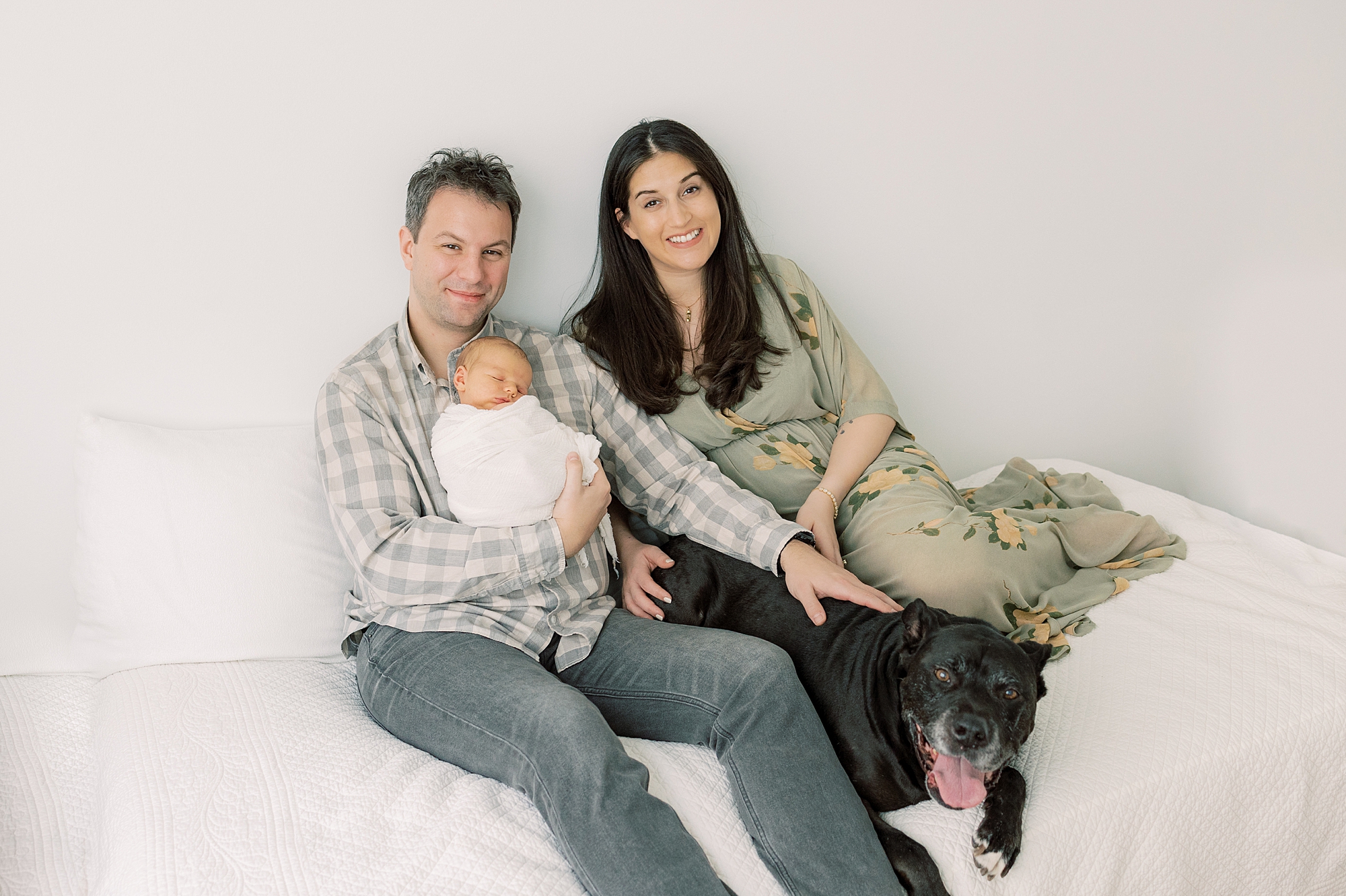 parents sit with elderly dog and newborn baby boy on bed during PA newborn portraits at home