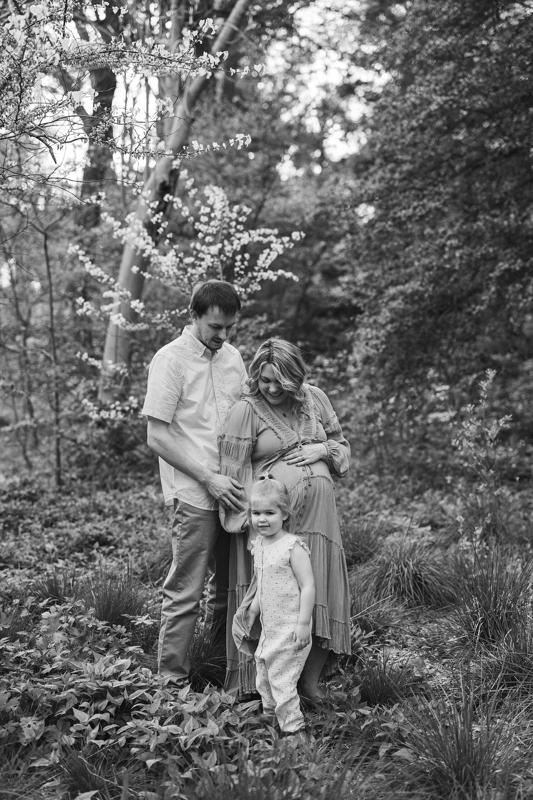black and white photo of parents standing with toddler in gardens during family photos 