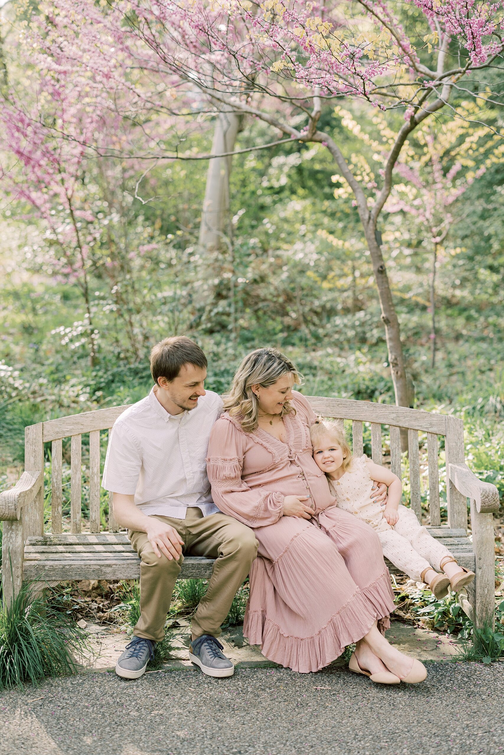 family sits together on wooden bench in garden during maternity photos in Philadelphia