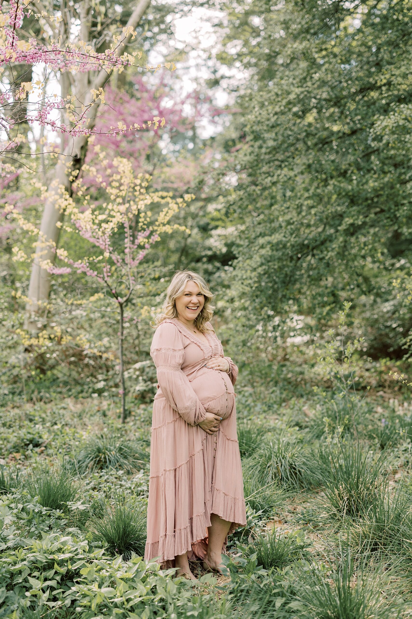 mom in pale pink dress holds baby bump standing in flowers at Longwood Gardens 