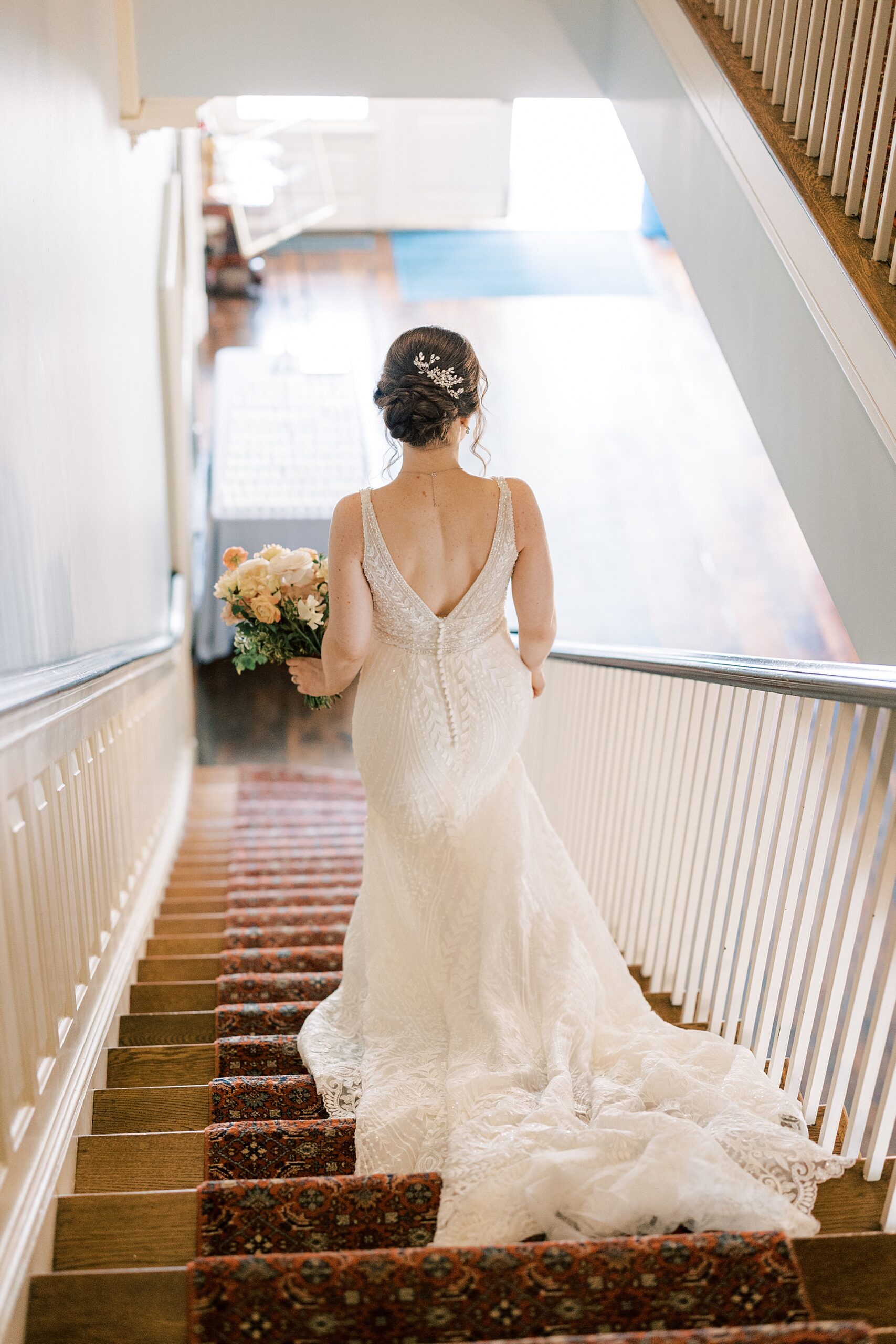 bride walks down staircase with wedding gown trailing at Bellevue Hall
