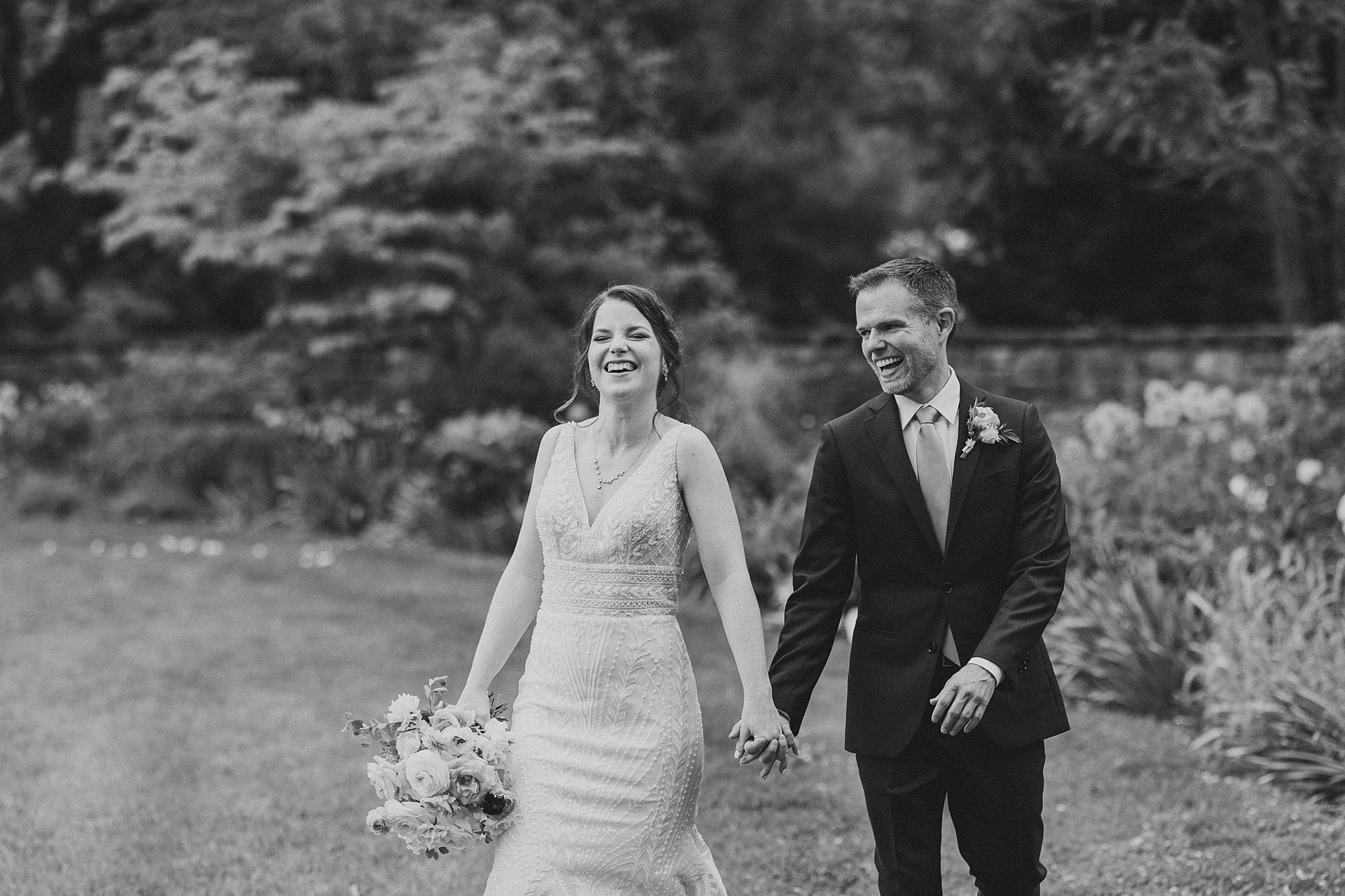 bride and groom laugh holding hands and walking through Bellevue Hall gardens in Wilmington DE
