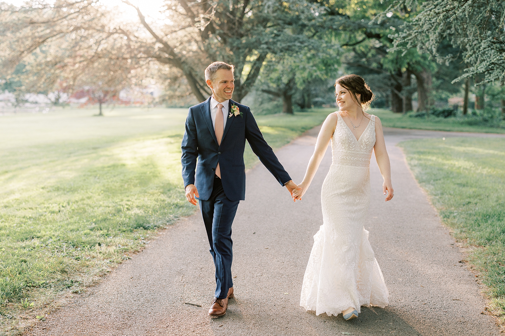newlyweds hold hands walking on path at Bellevue Hall