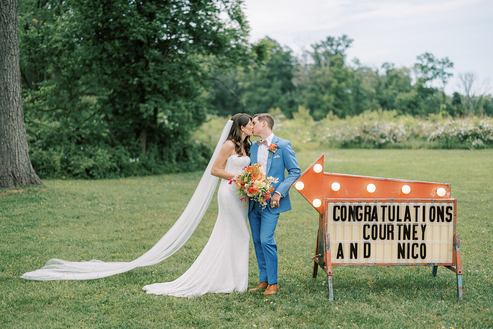 bride and groom hug by custom 70s inspired sign on lawn at Bowman's Hill Wildflower Preserve wedding