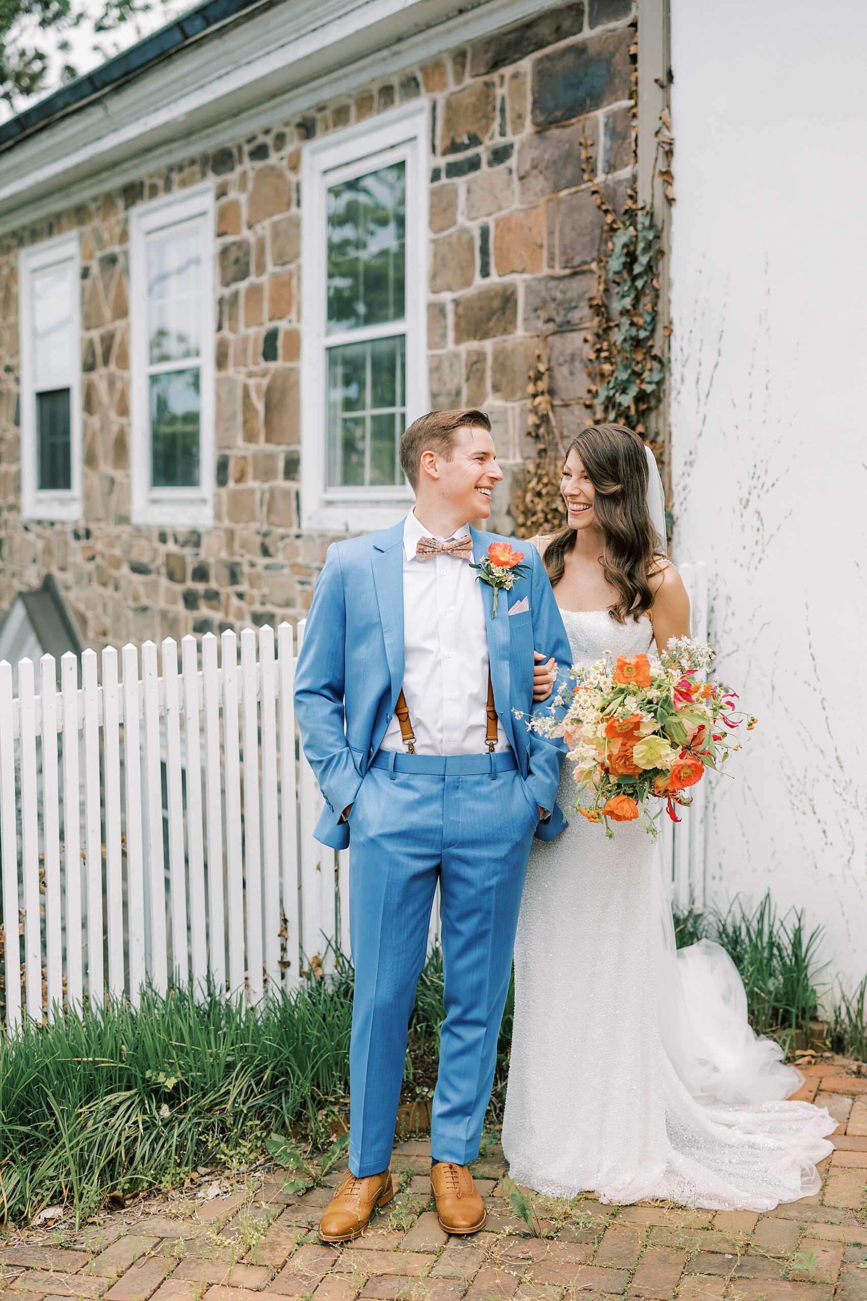 bride and groom pose by white fence and stone wall in downtown New Hope PA