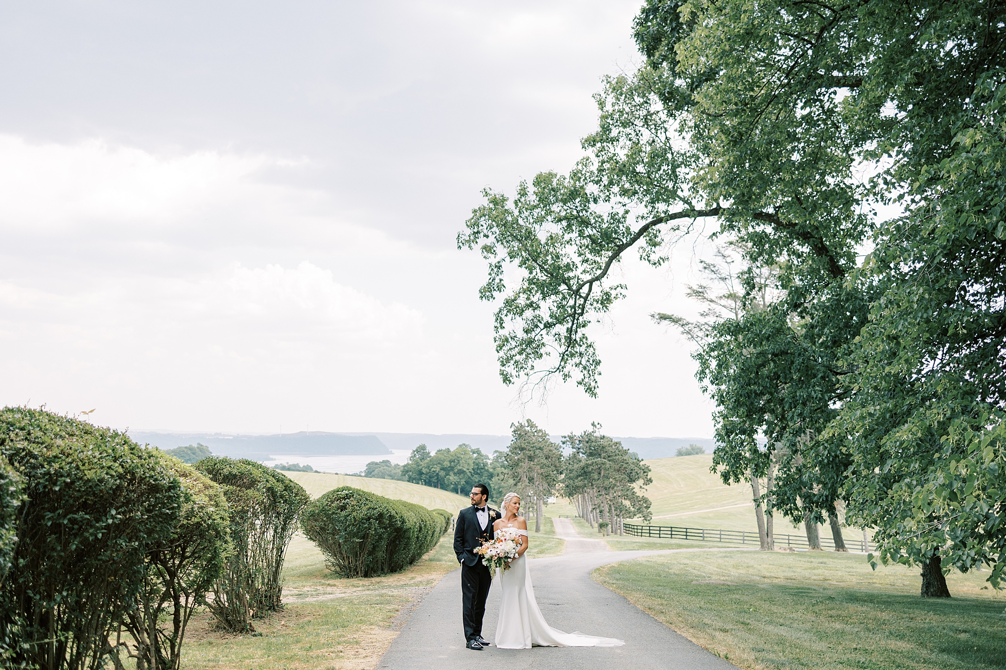 bride and groom stand on driveway hugging during summer wedding at Lauxmont Farms