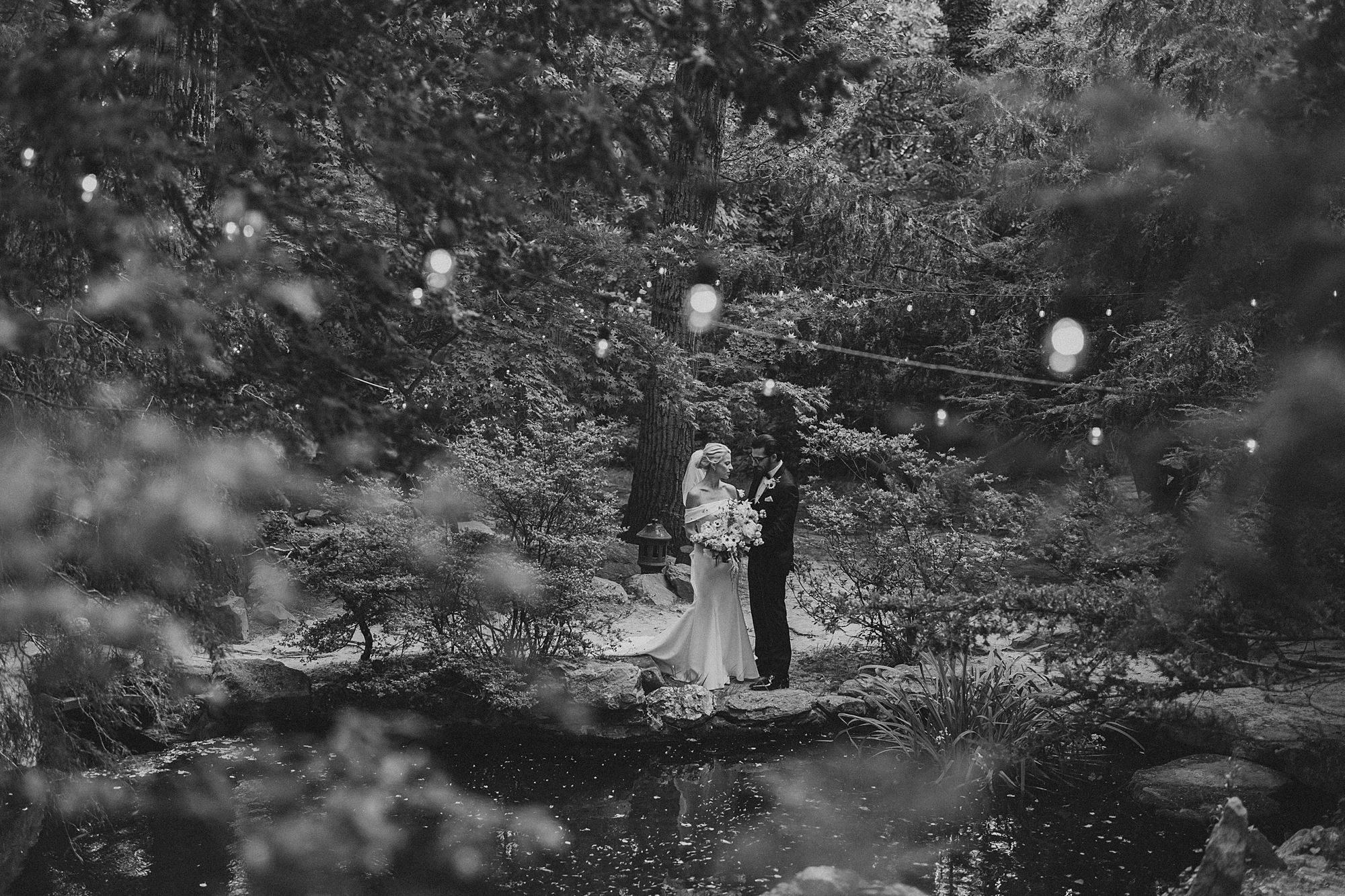 black and white portrait of bride and groom on stone wall on pond at Japanese Gardens at Lauxmont Farms
