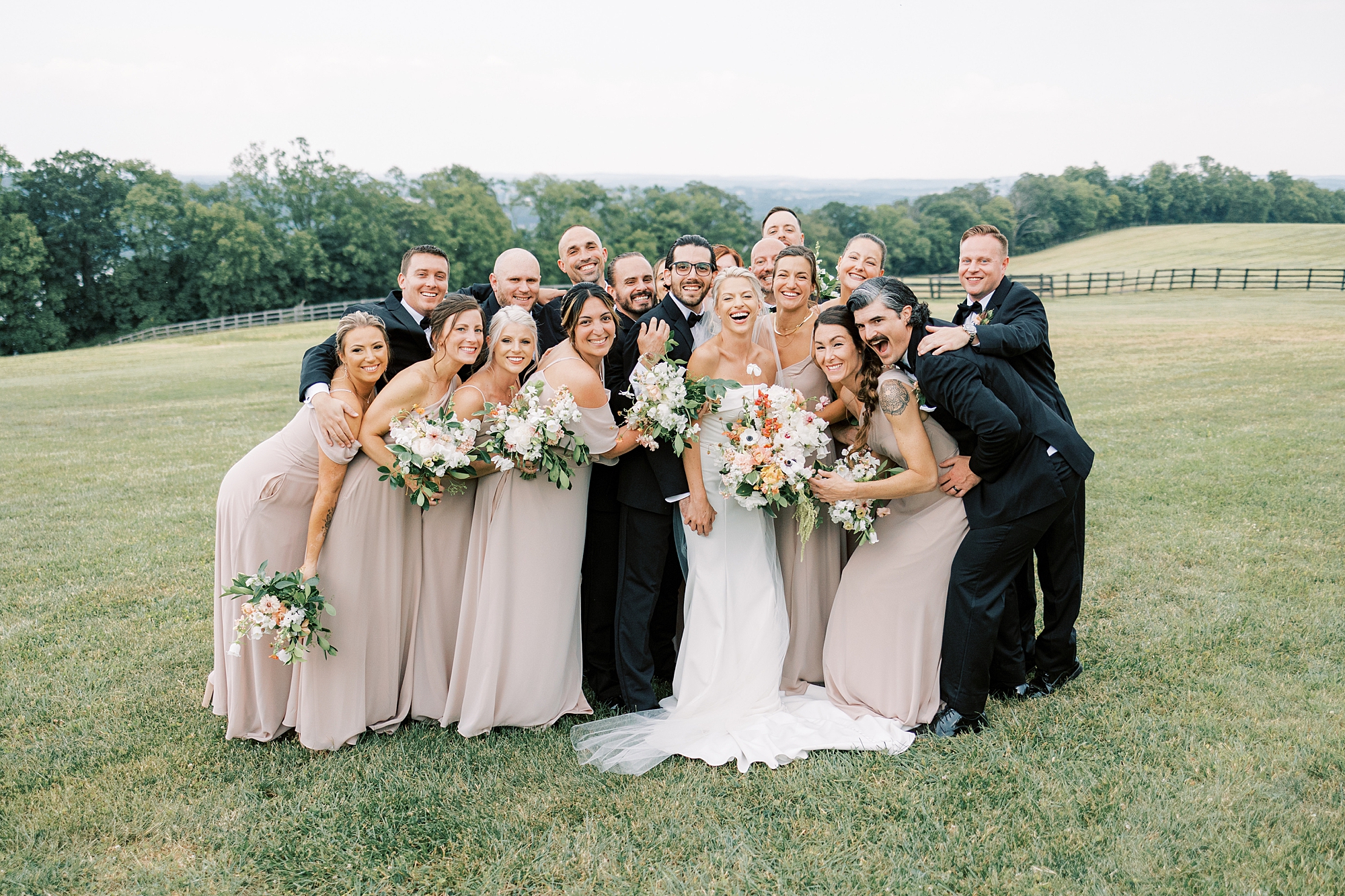 bride and groom hug with bridal party in black suits and pink gowns