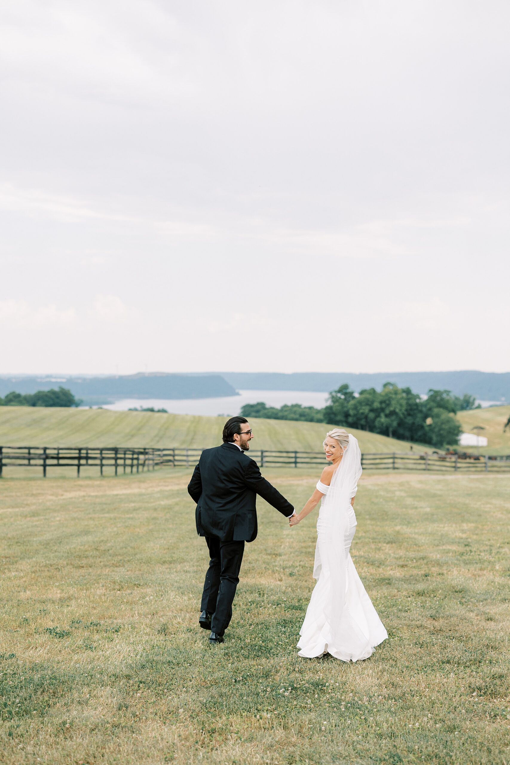 bride and groom hold hands walking towards mountains on lawn at Lauxmont Farms
