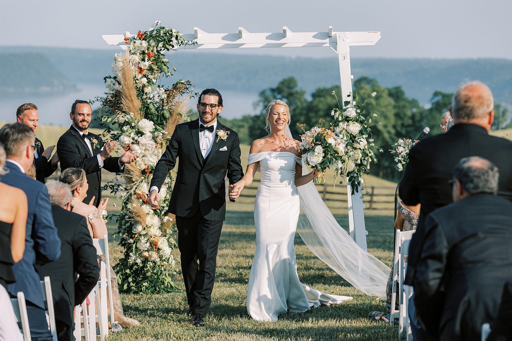 newlyweds walk down aisle in front of mountains during ceremony on lawn at Lauxmont Farms