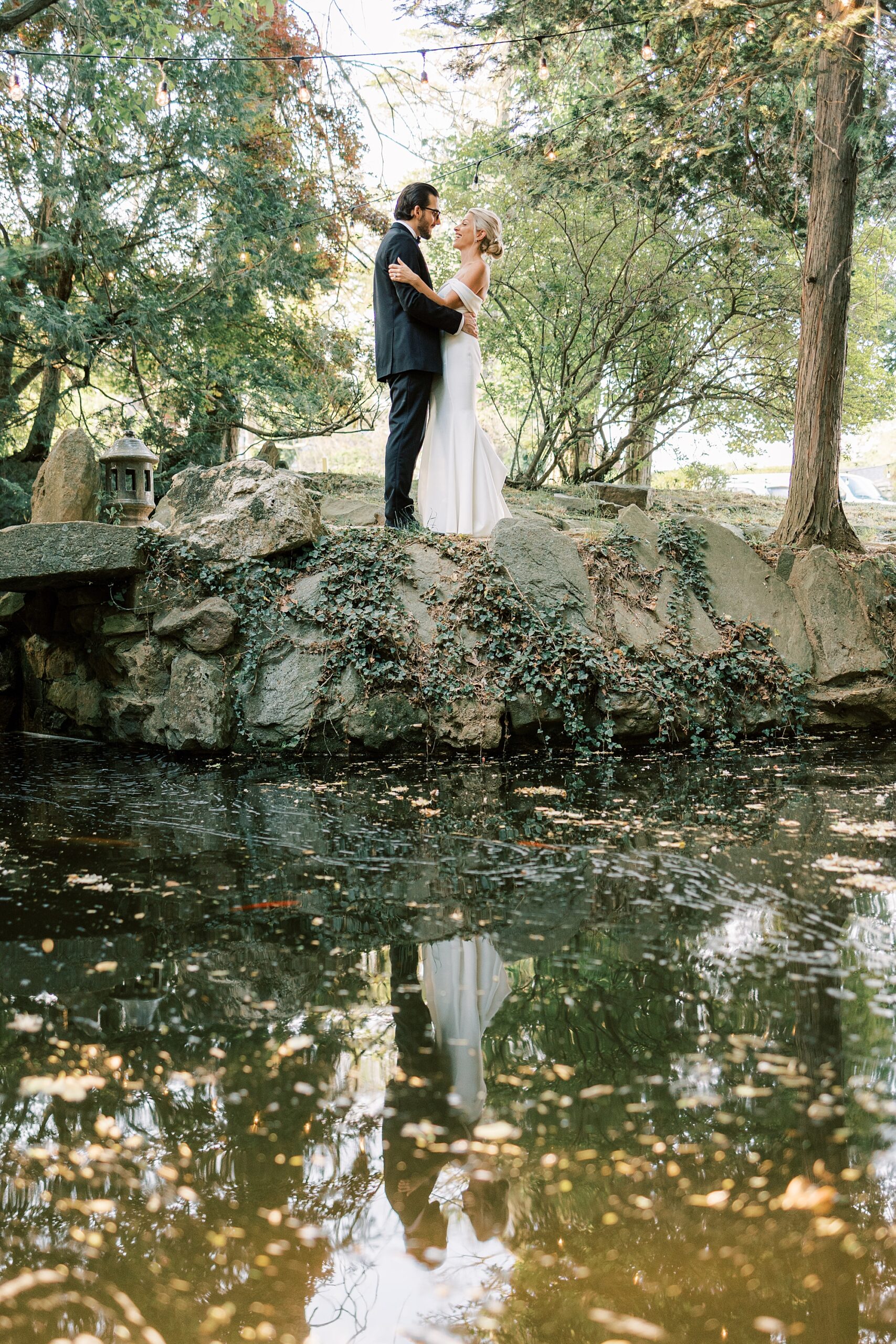 newlyweds hug on stone wall overlooking Japanese Gardens