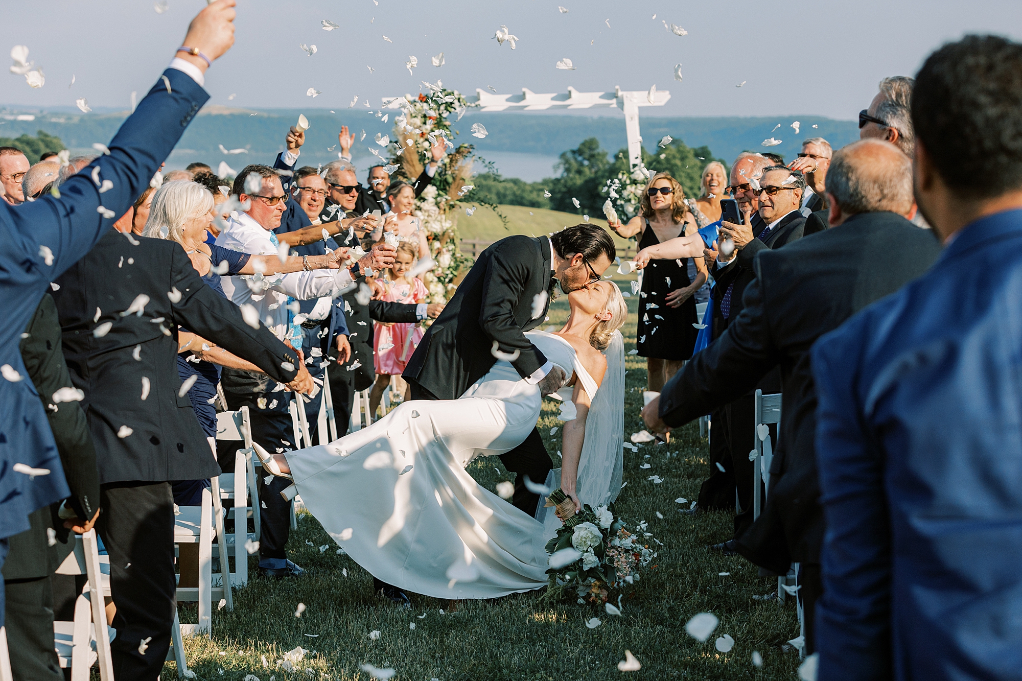 groom kisses bride while guests toss flower petals at Lauxmont Farms