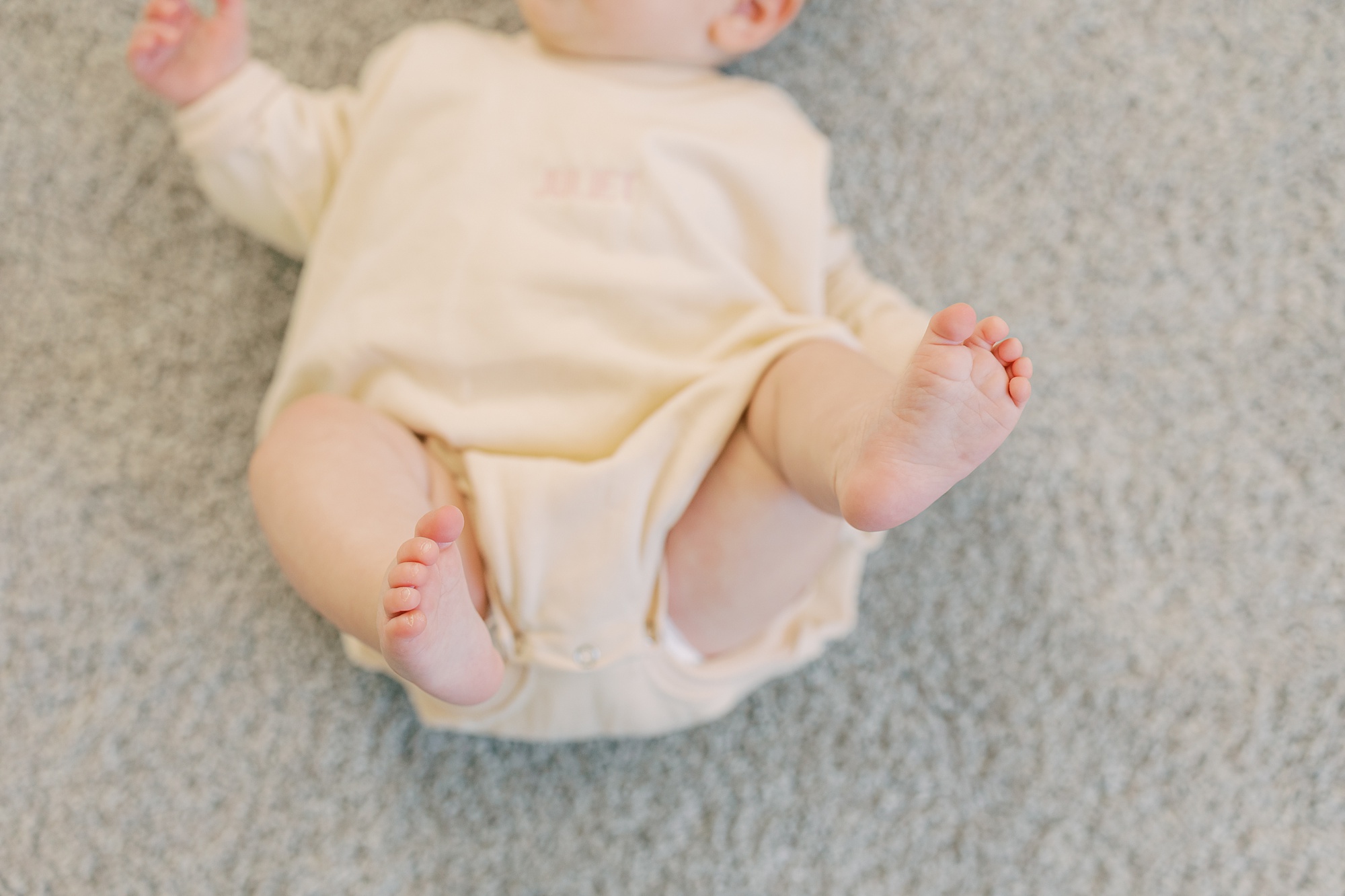 baby lays on floor of nursery in cream colored sweater 