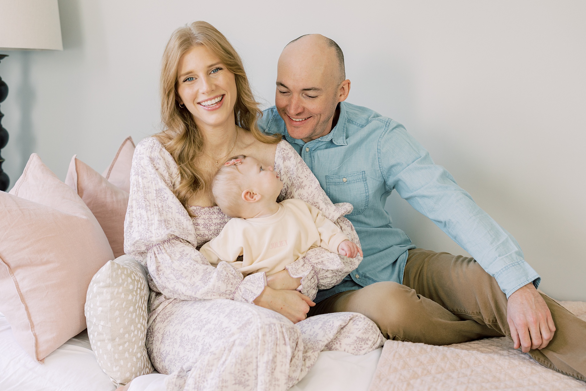 parents smile at daughter in mom's lap on bed during lifestyle milestone portraits