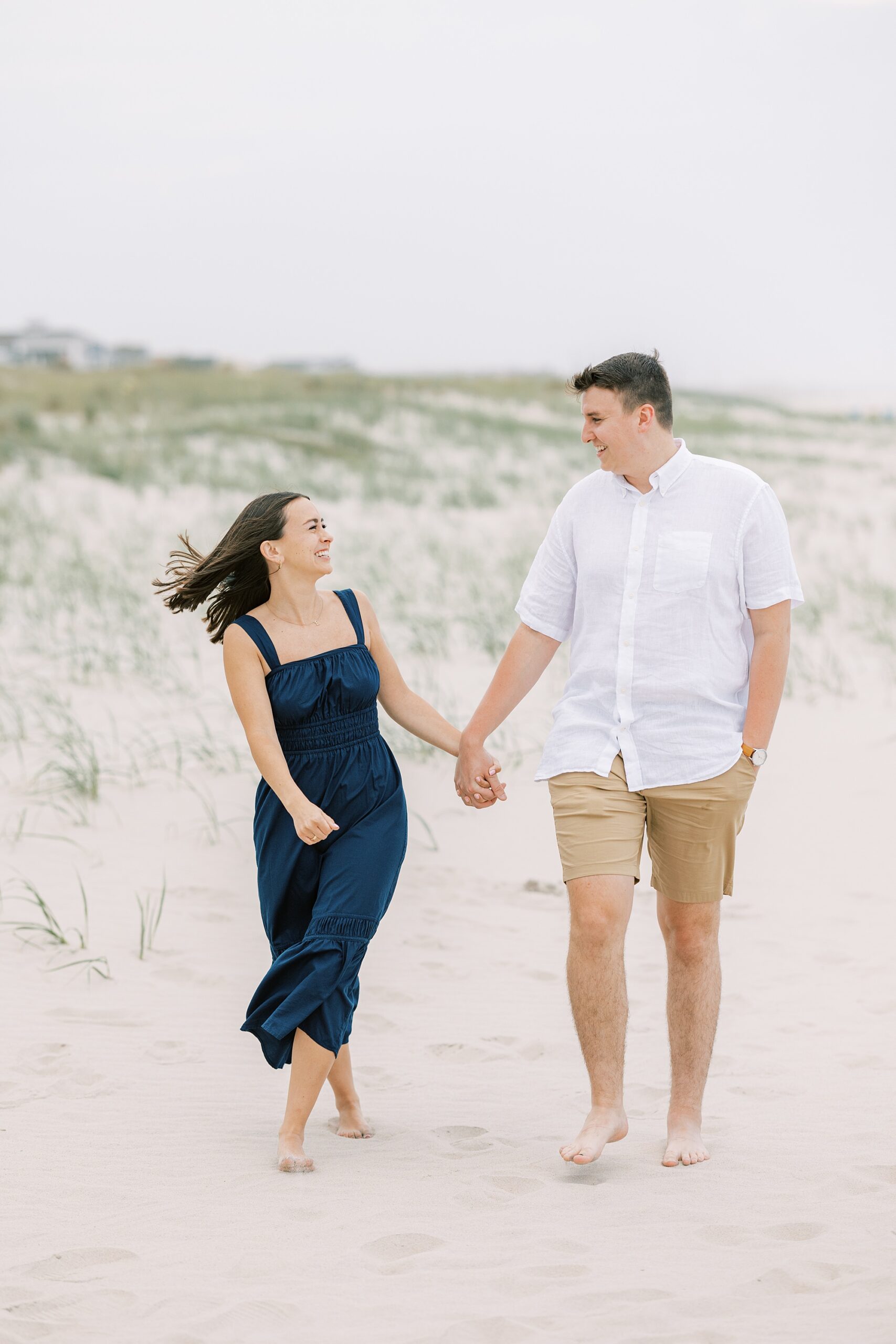 engaged couple holds hands walking on beach near dunes