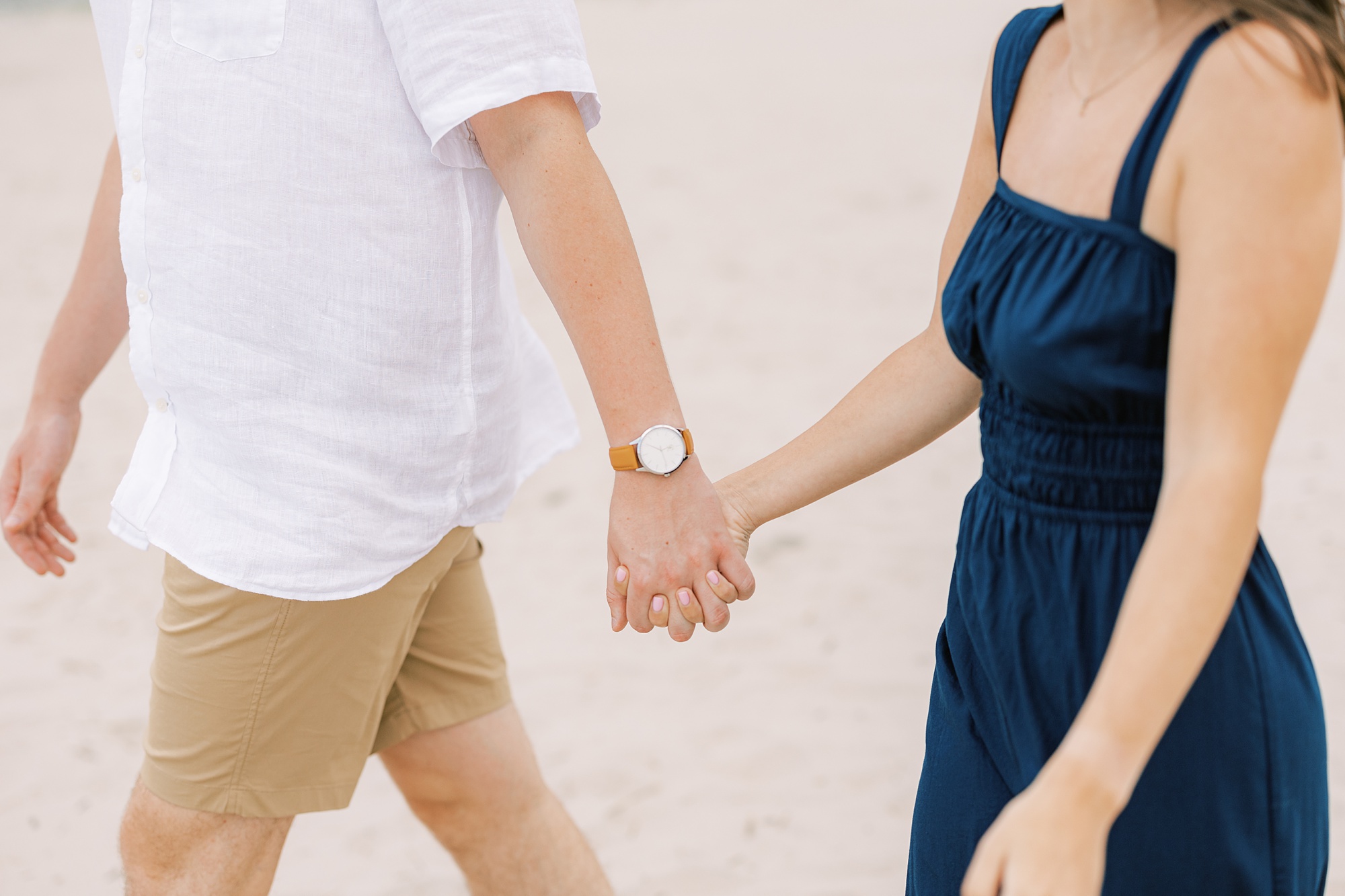 man and woman hold hands walking on beach during windy day