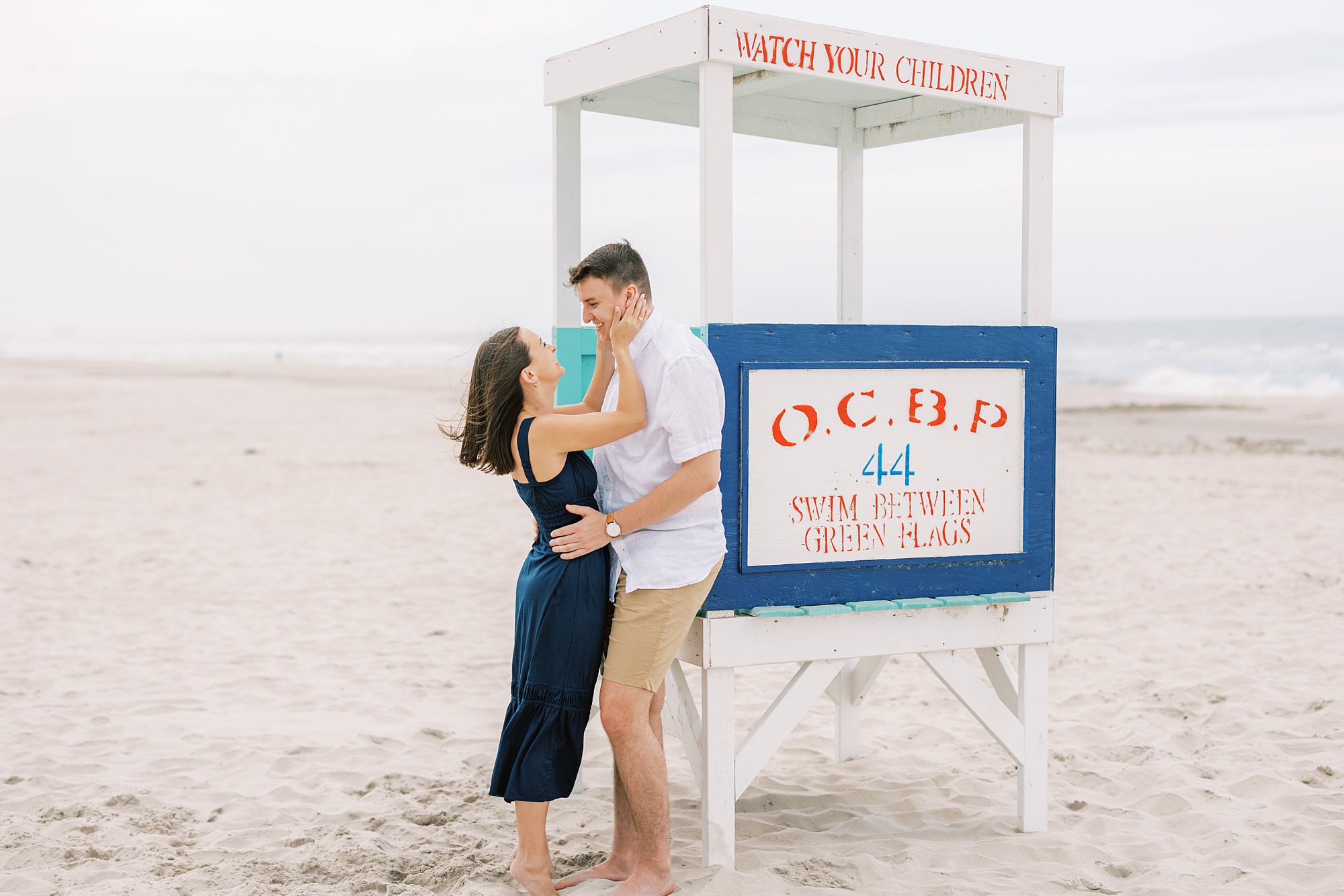 woman looks up at man holding his cheek during beach engagement session in New Jersey 