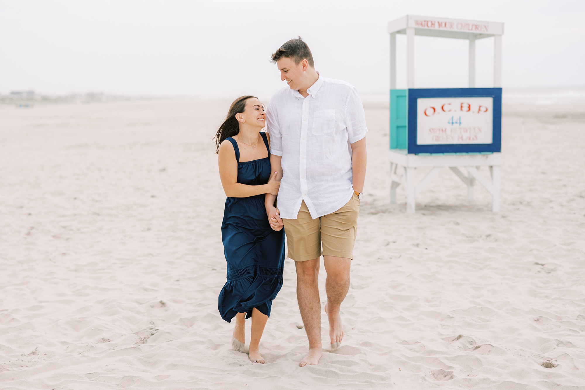 woman looks up at man holding his hand near lifeguard stand during Ocean City NJ engagement photos