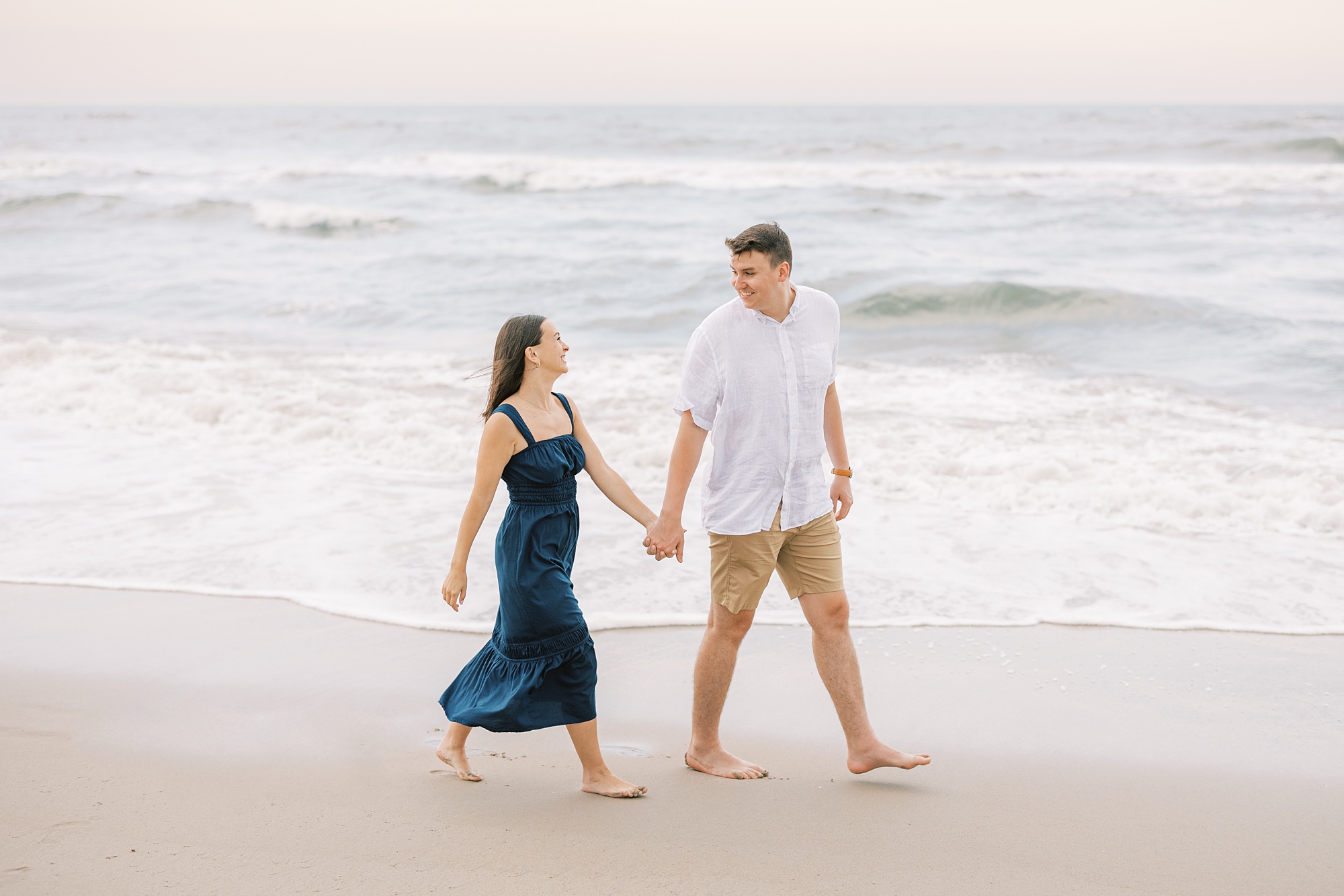 bride and groom hold hands walking along water during Ocean City NJ engagement photos