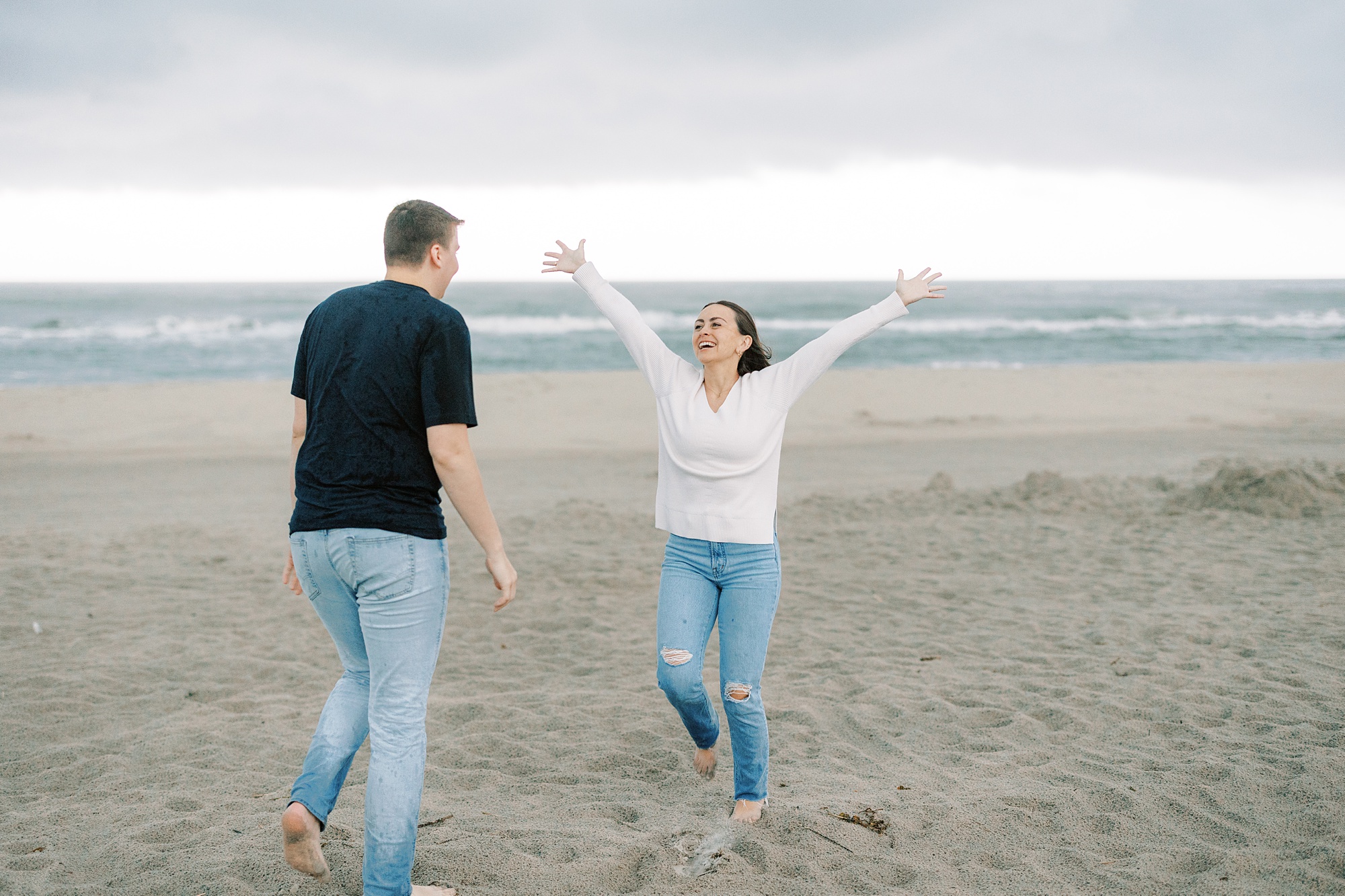 woman cheers during Ocean City NJ engagement photos on beach during storm