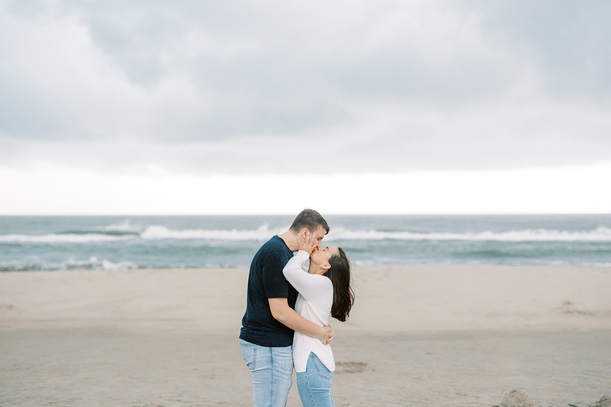engaged couple kisses in front of water on beach during storm