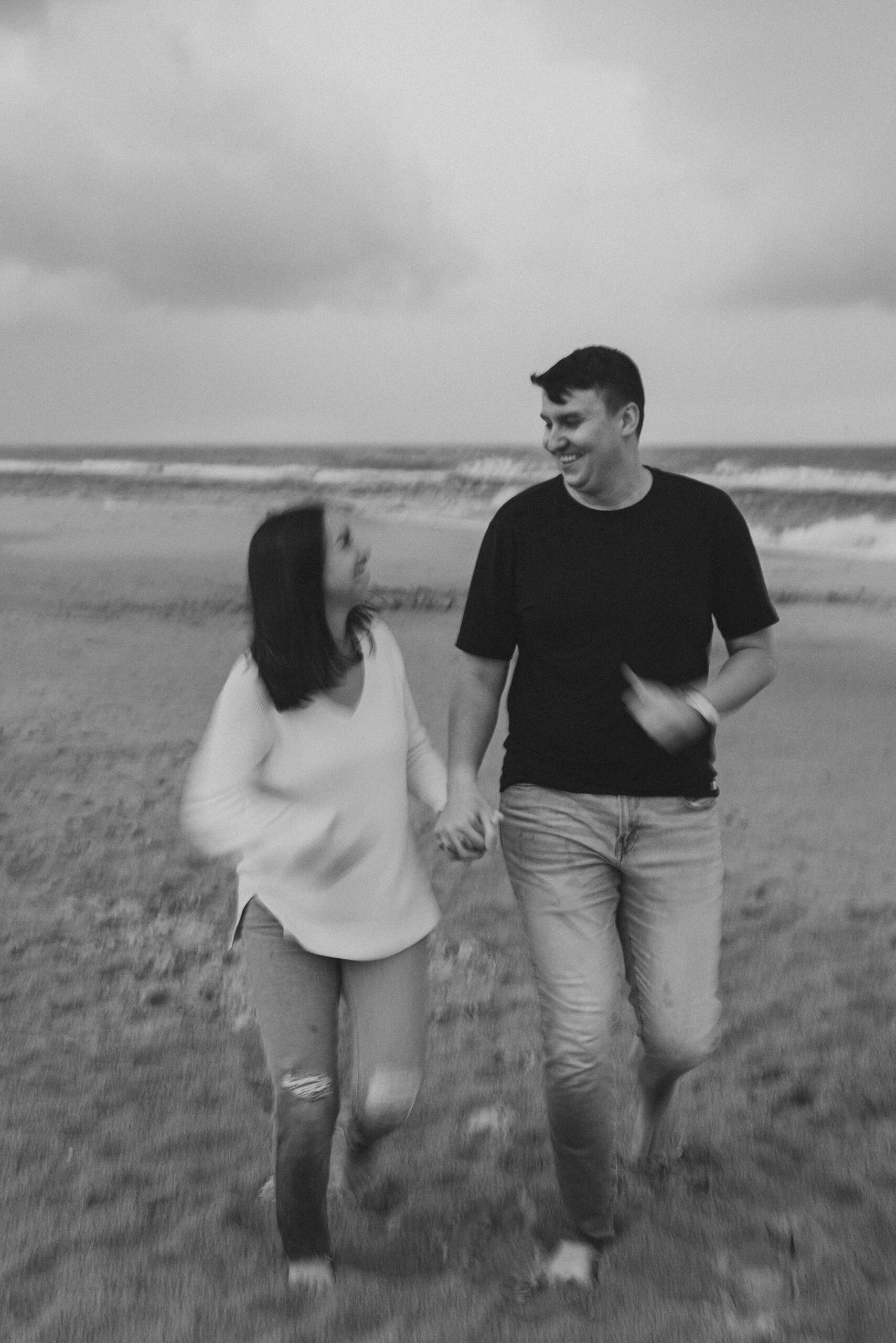 black and white photo of couple running on beach