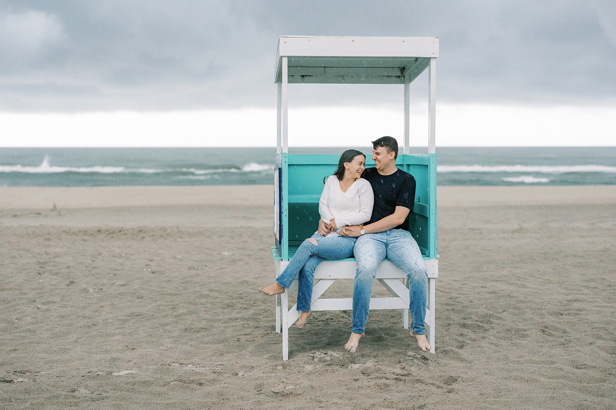 engaged couple sits in lifeguard stand during rainy day