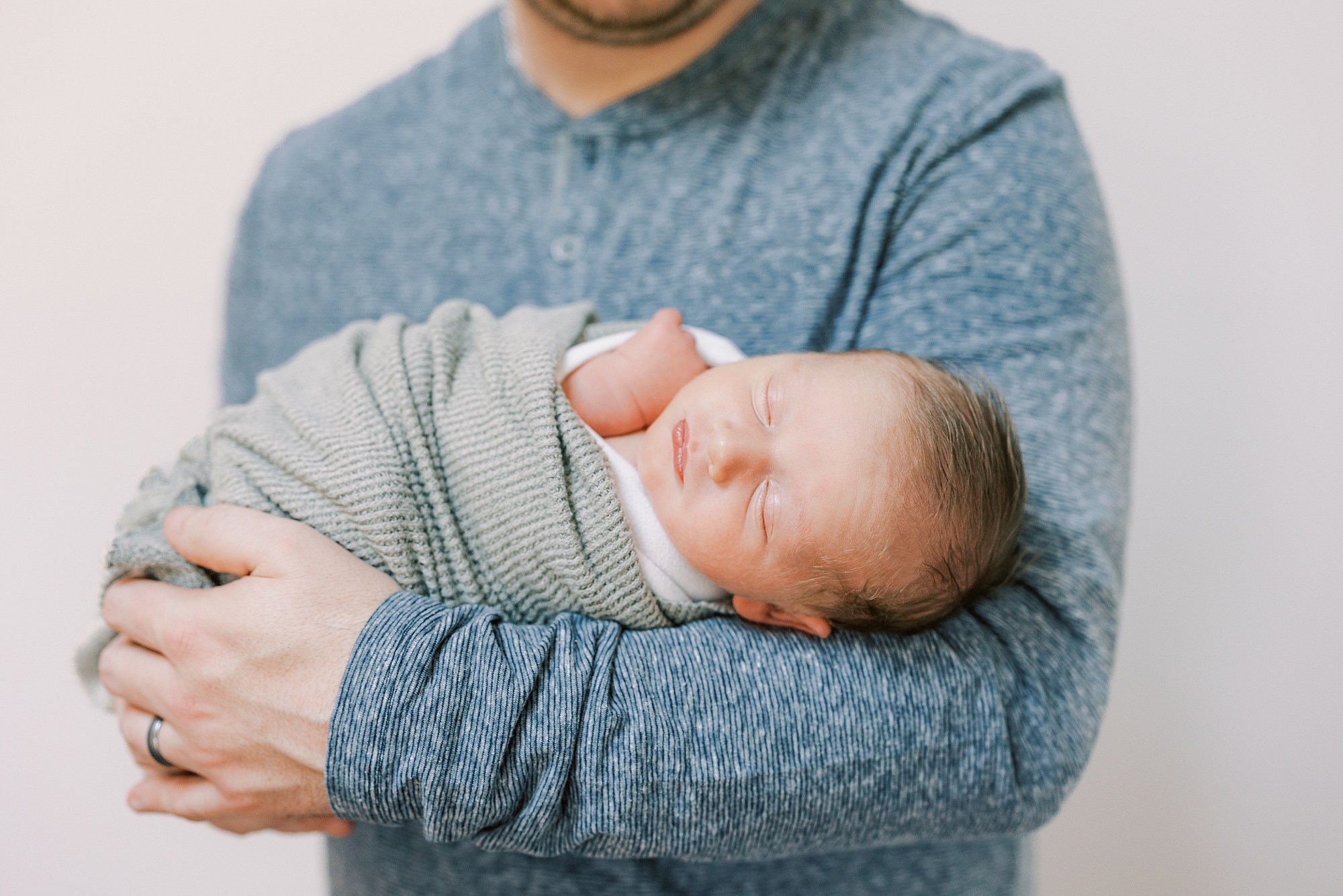dad holds son in arms while he sleeps in green wrap