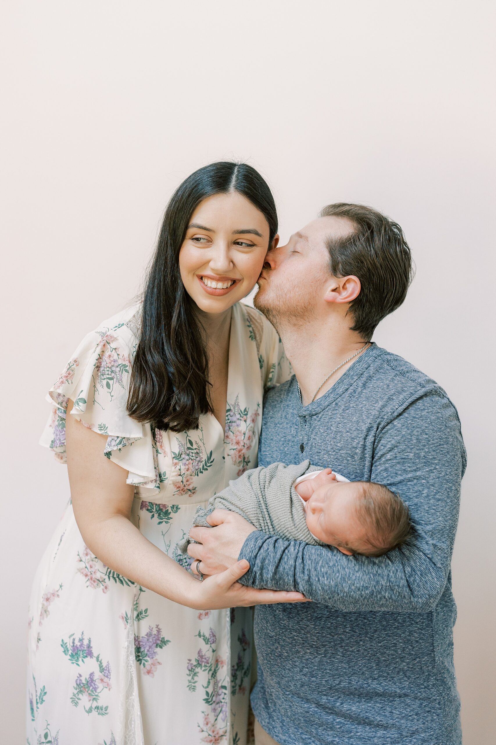 dad holds son in arms while kissing wife's cheek during Philadelphia newborn portraits