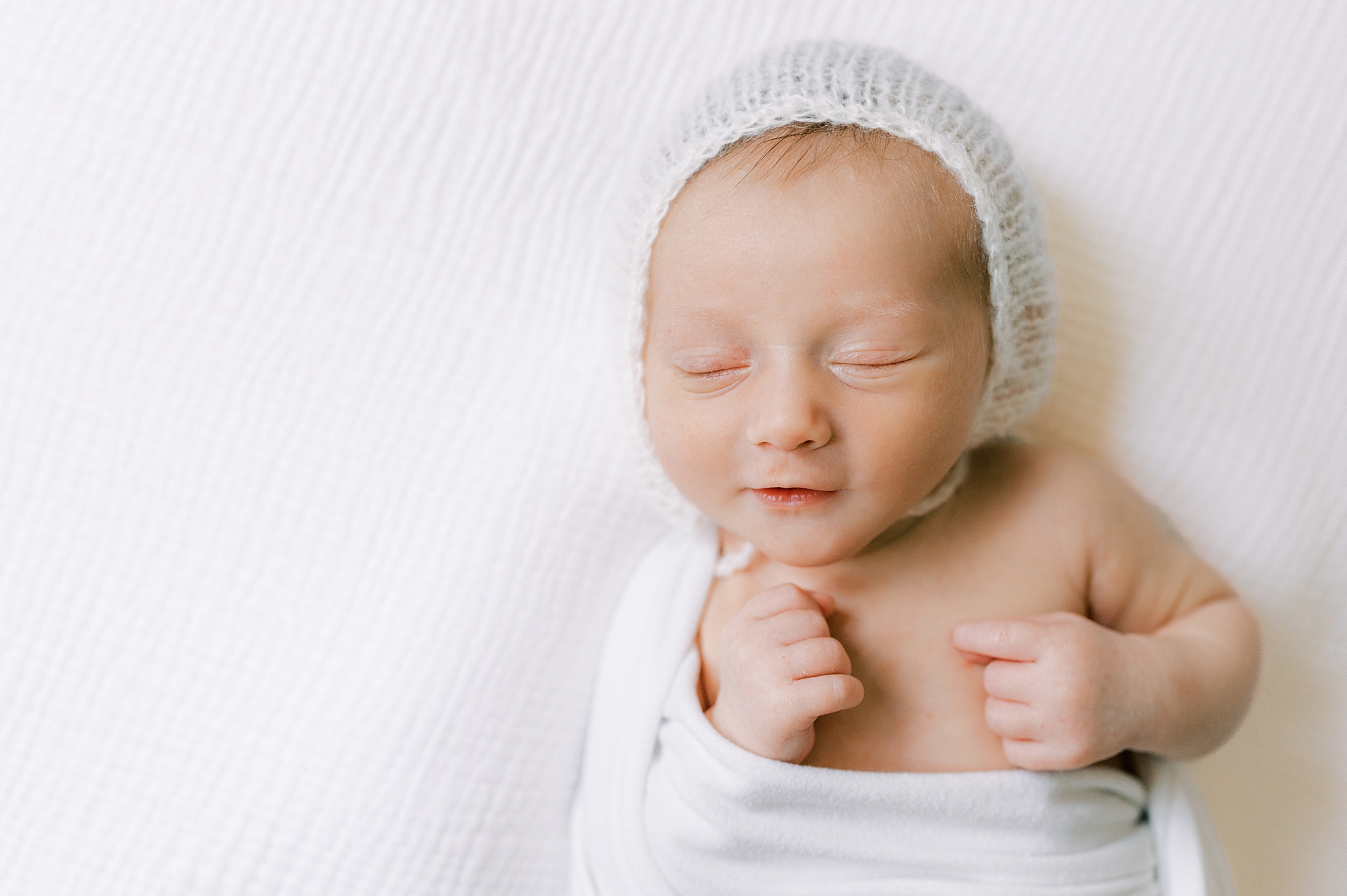 baby lays on bed in white wrap and knit cap during PA newborn photos 