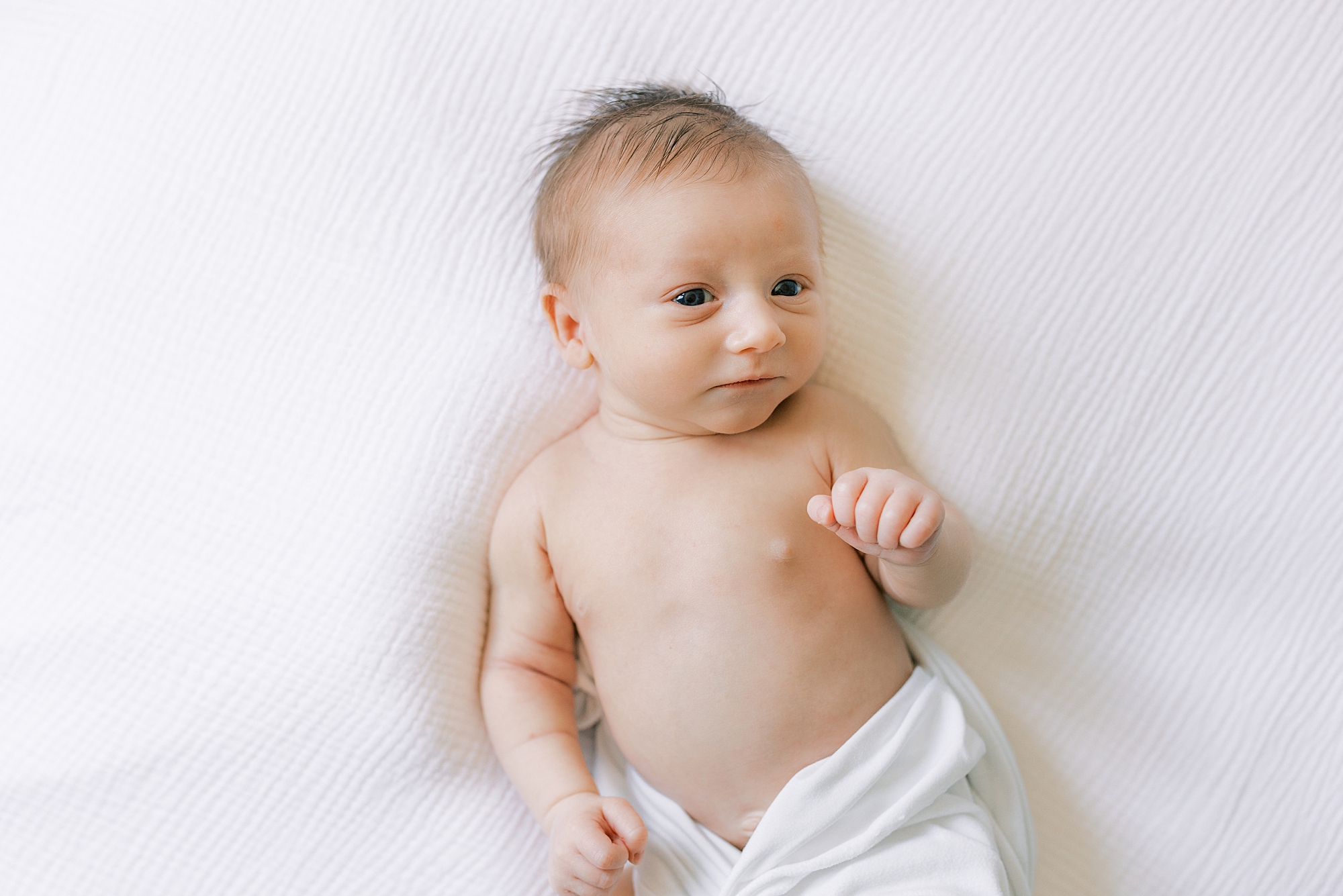 baby lays in white wrap on bed during lifestyle Philadelphia newborn portraits