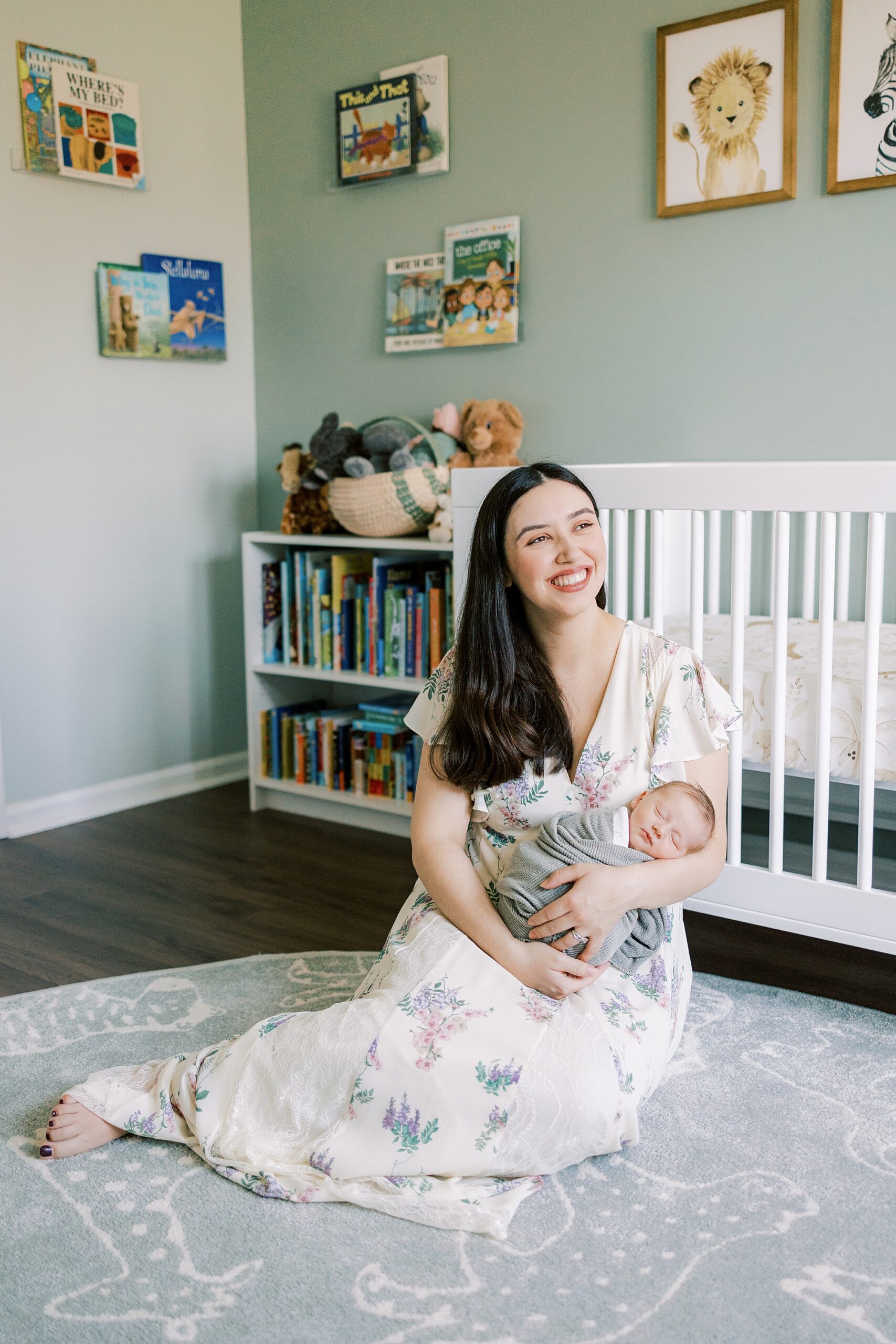 mom sits on nursery floor in front of crib holding son