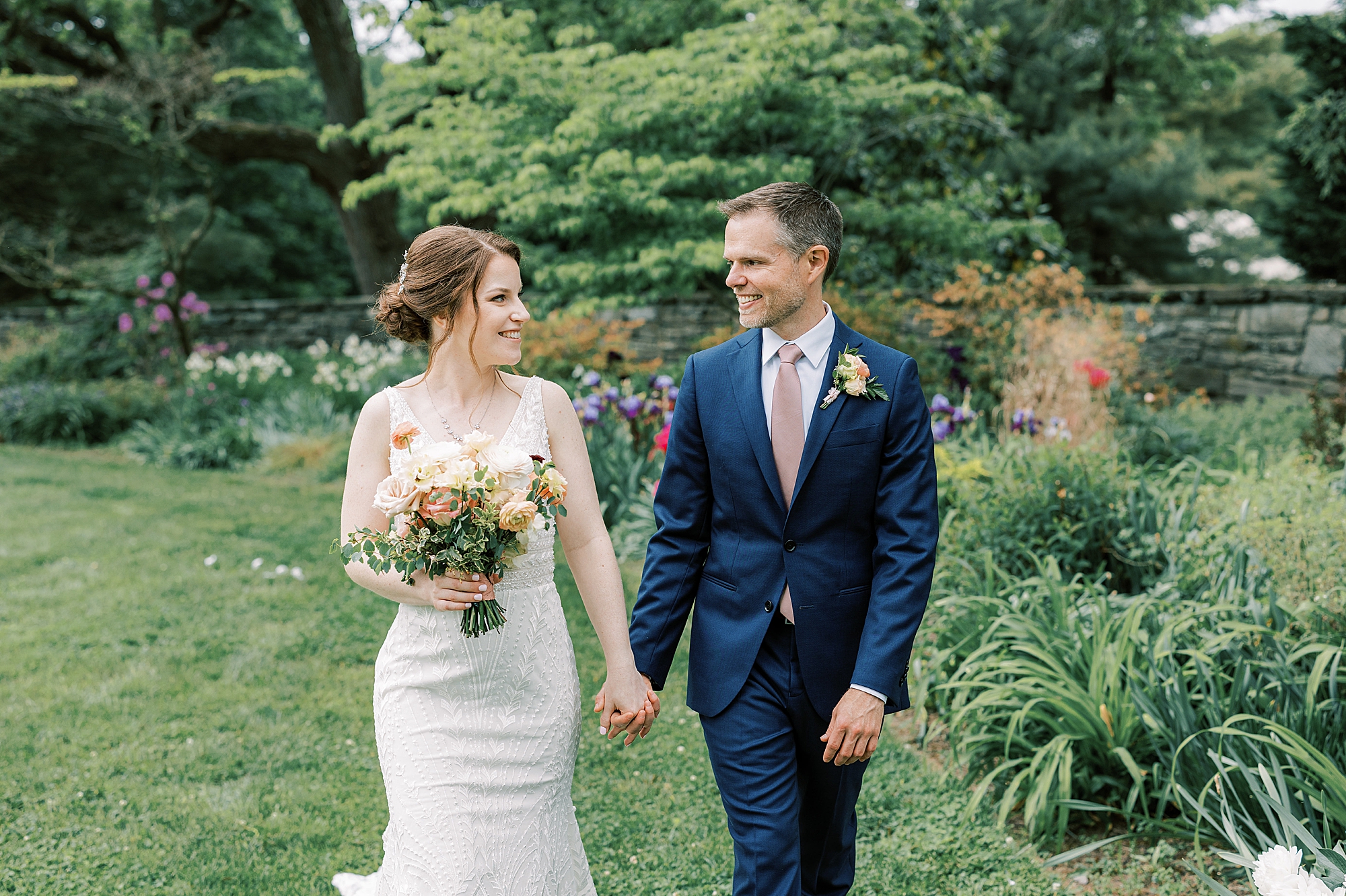 bride and groom hold hands walking together through Bellevue Hall gardens