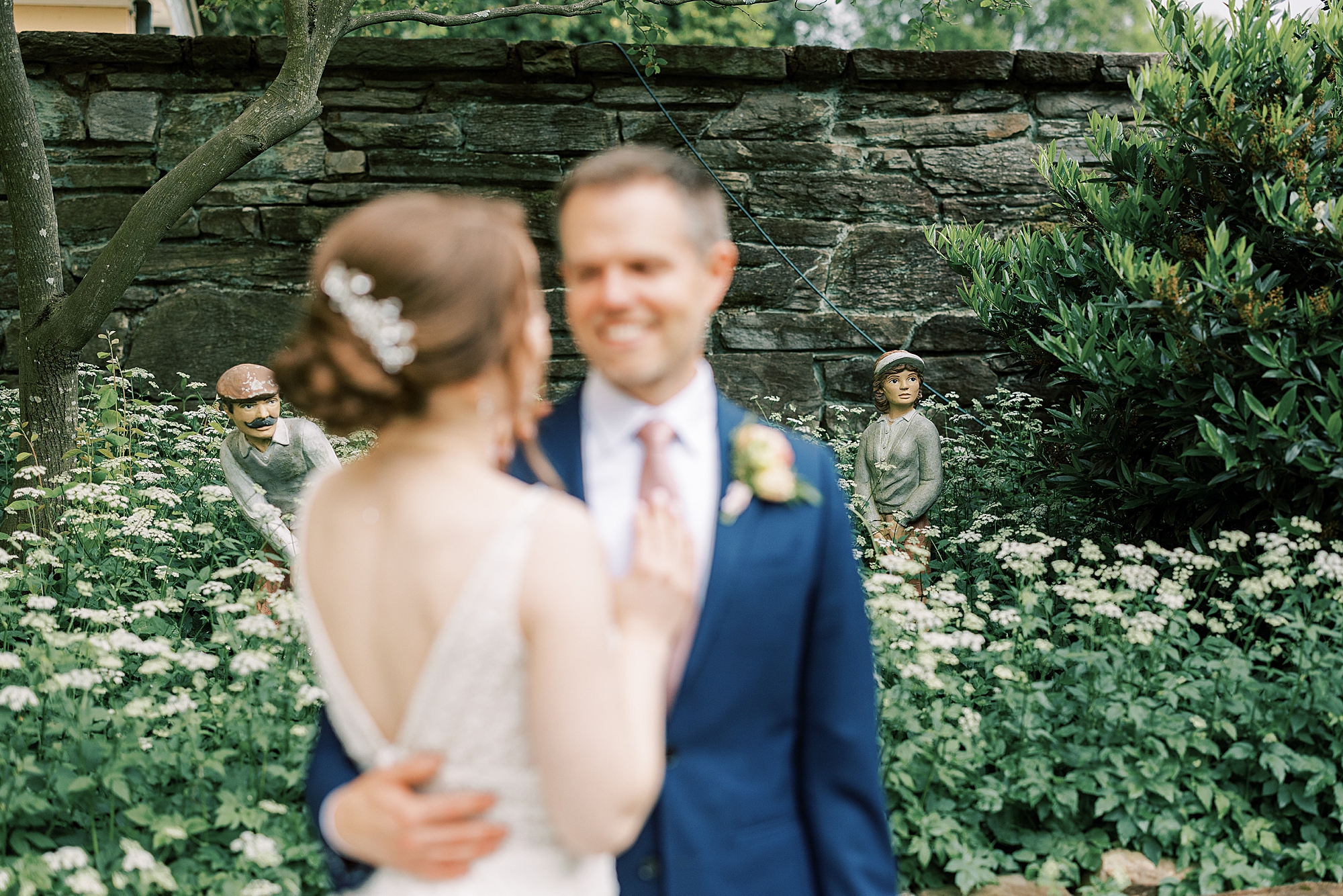 bride and groom smile surrounded by statutes in garden 