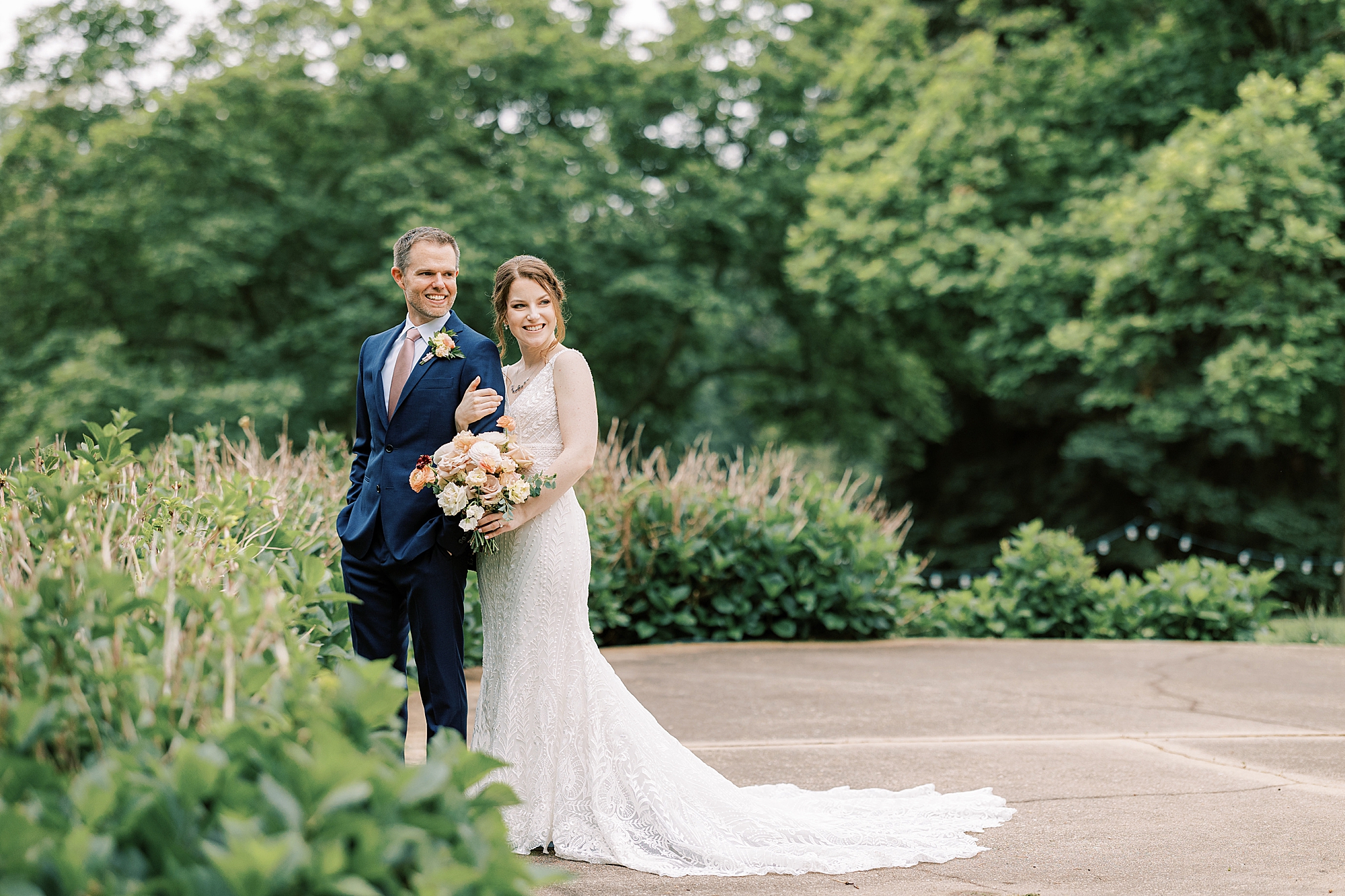 bride and groom smile hugging near bush in Bellevue Hall gardens