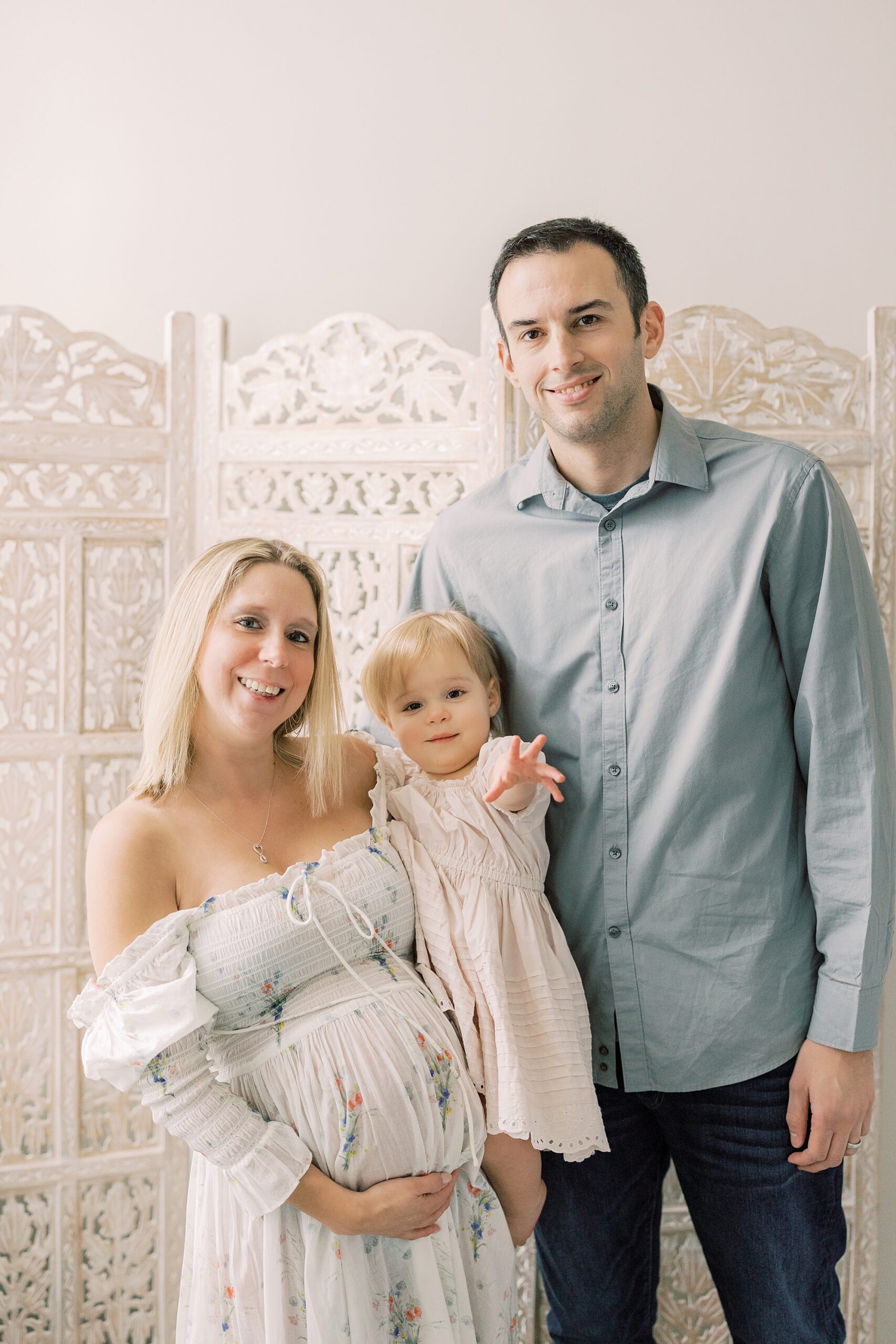 parents stand with toddler in front of wall divider during studio maternity session in Media PA