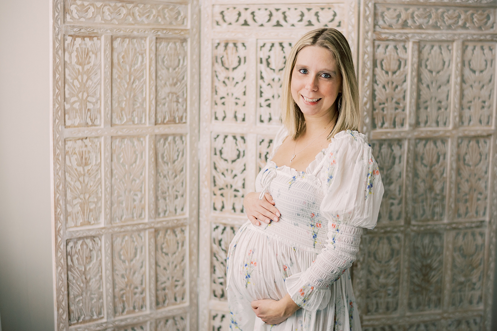 mom stands in front of textured wall divider holding baby bump during studio maternity session in Media PA