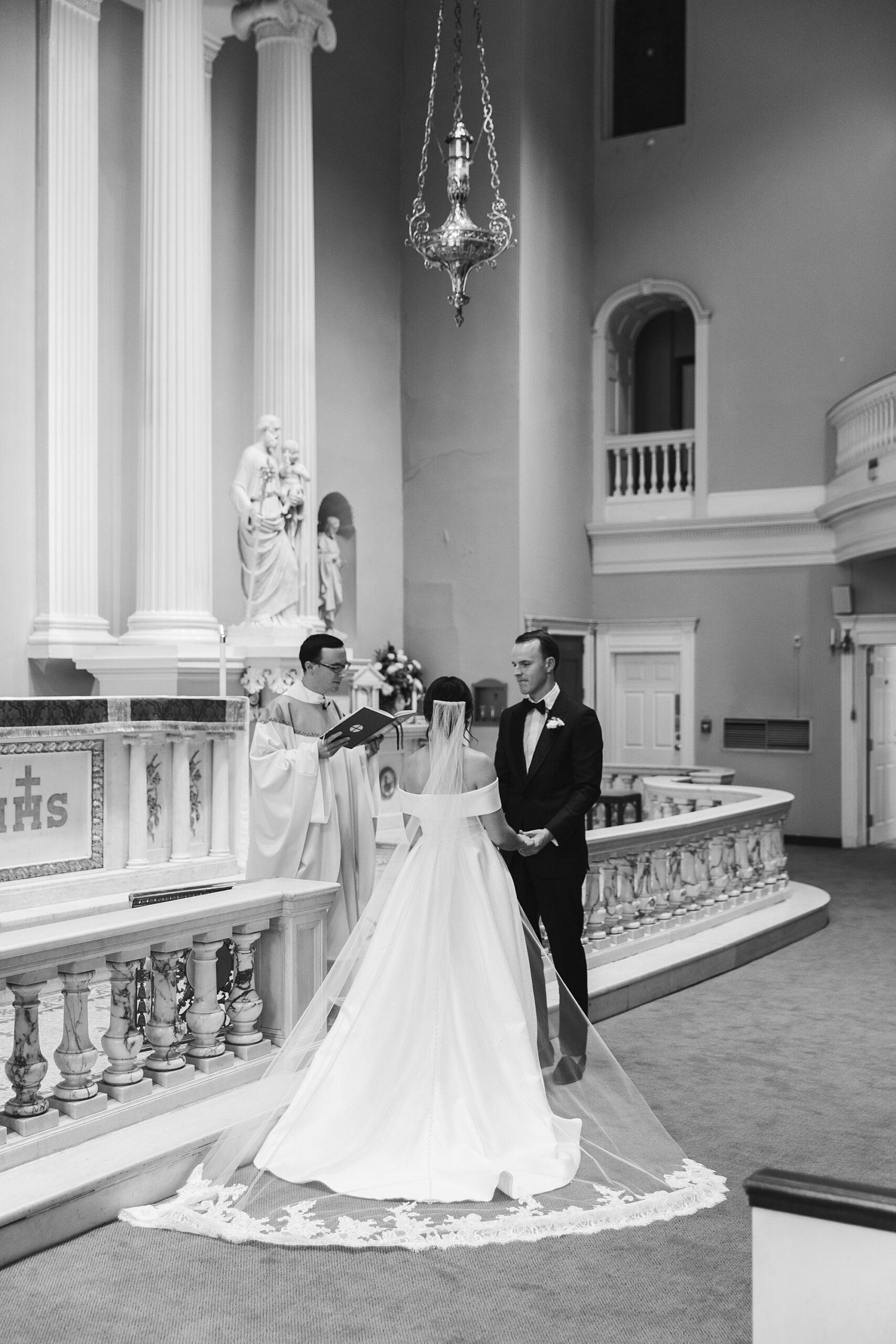 bride and groom listen to priest during ceremony at Old St. Joseph’s Catholic Church in Philadelphia PA