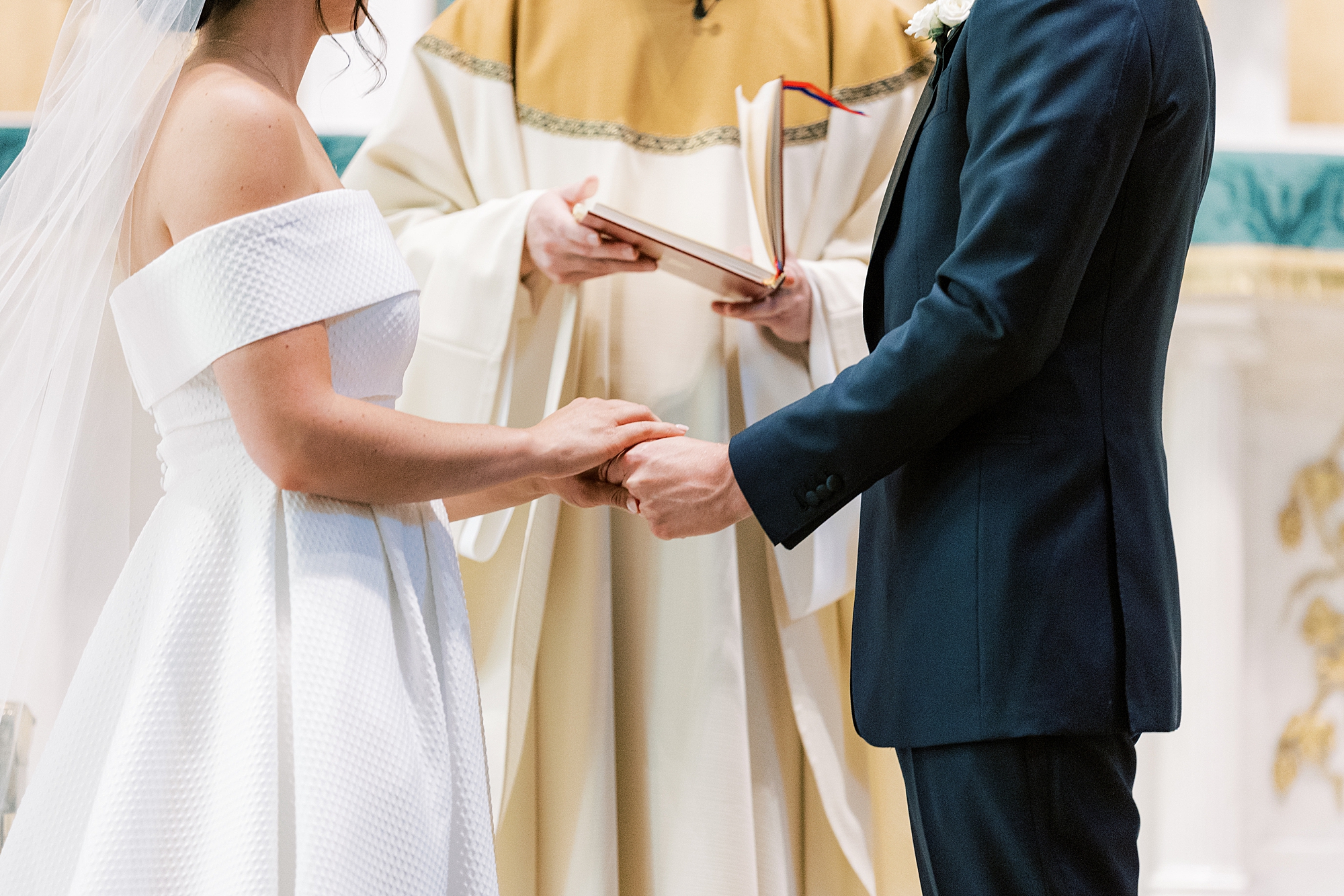 bride and groom hold hands in front of priest at Old St. Joseph’s Catholic Church in Philadelphia PA