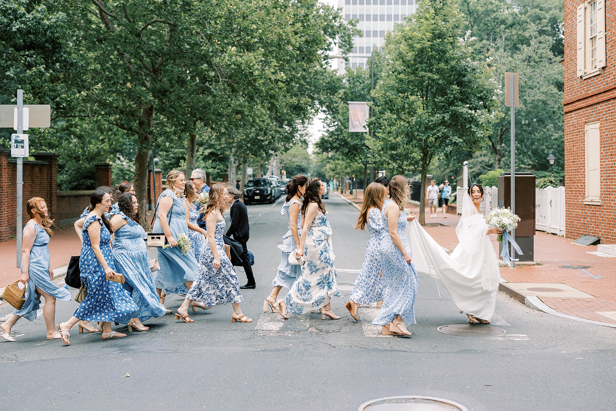 bridesmaids in blue gowns help bride cross street in wedding dress