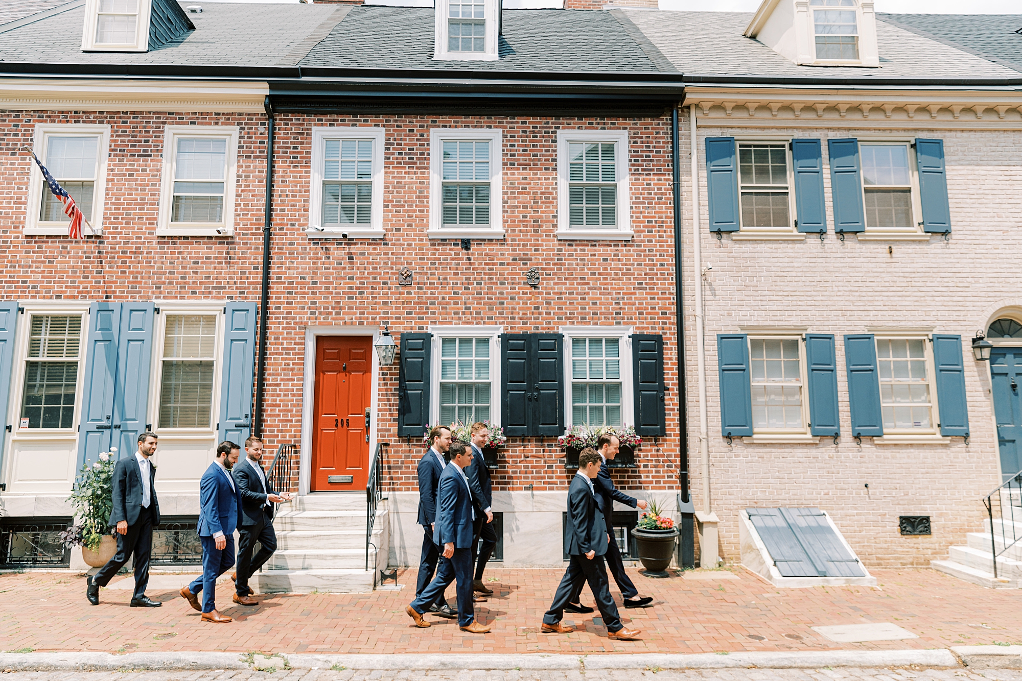 groom and groomsmen walk in front of brick houses in Philadelphia PA