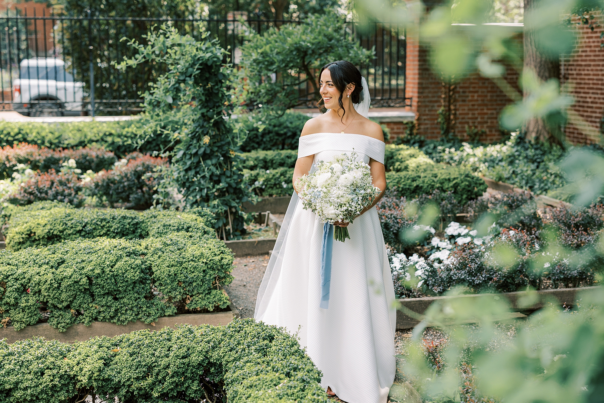 bride walks through gardens carrying bouquet of white flowers with blue ribbon in Philadelphia 