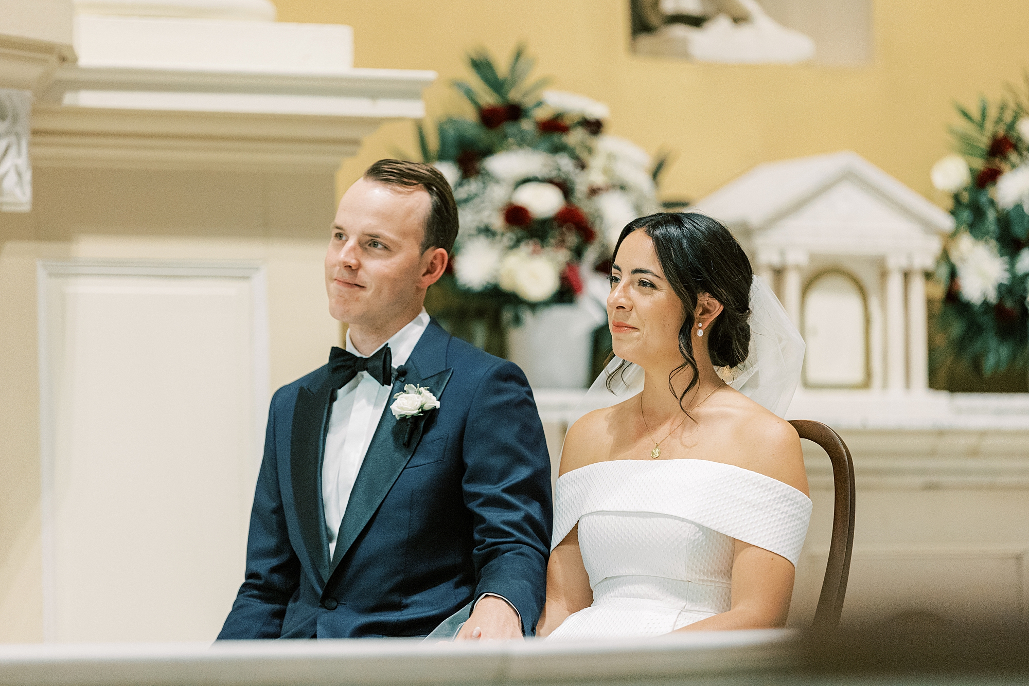 bride and groom sit in pew listening during ceremony at Old St. Joseph’s Catholic Church in Philadelphia PA