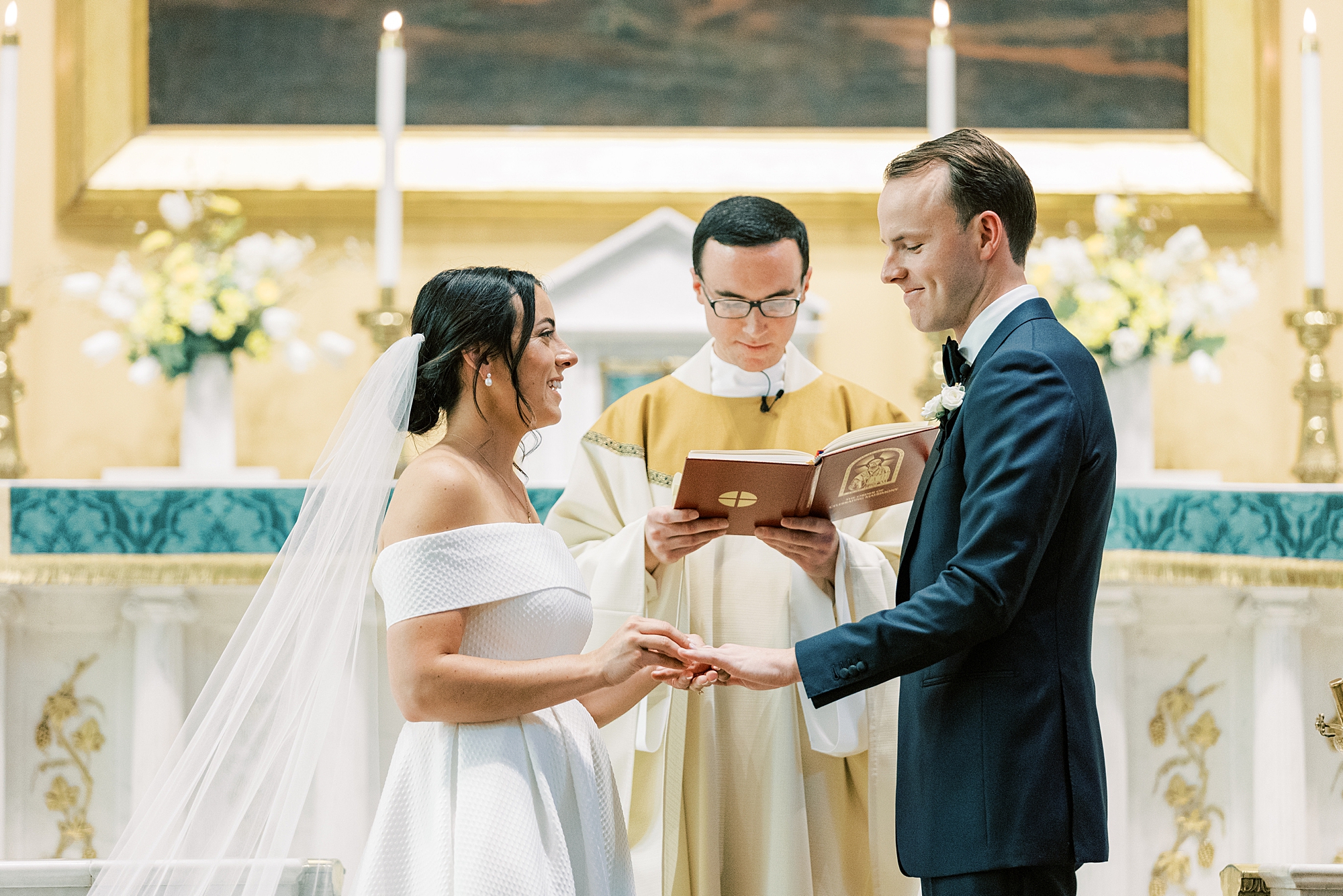 bride smiles as she puts groom's ring on during wedding ceremony at Old St. Joseph’s Catholic Church in Philadelphia PA