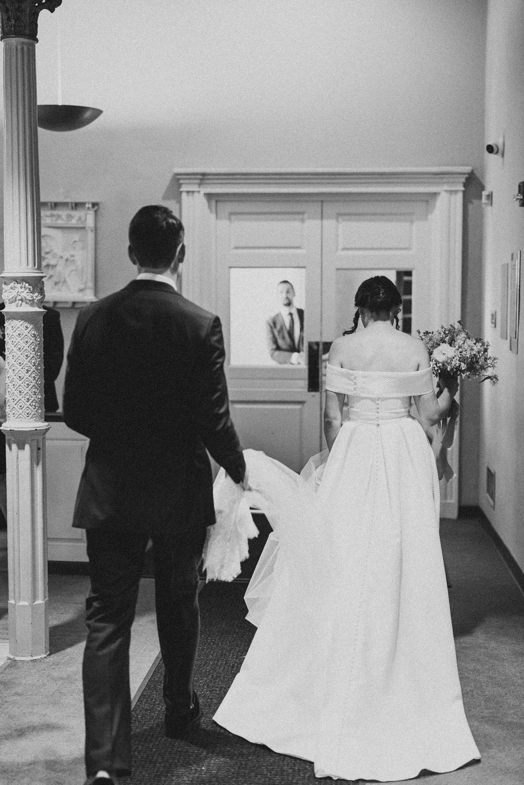 groom helps bride carry dress out of Old St. Joseph’s Catholic Church in Philadelphia PA