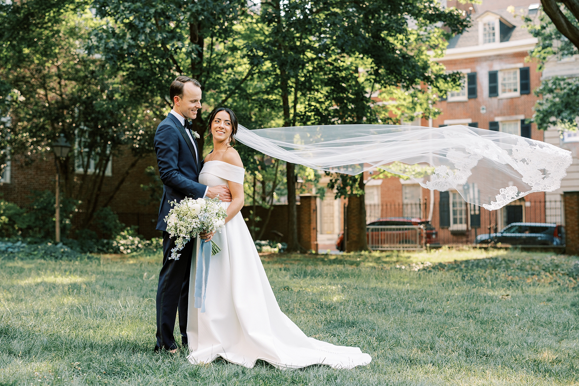 Bride's cathedral length veil blows in the wind as she embraces her groom during their Philadelphia wedding photos