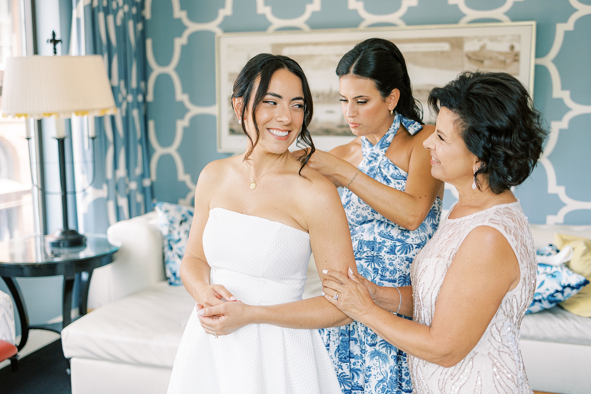 bride smiles at mother while sister helps her into wedding gown