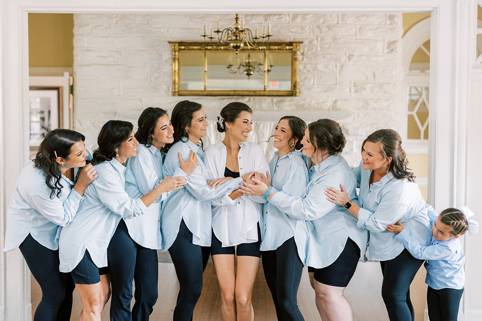 bride poses with bridesmaids in blue shirts before Philly wedding day 