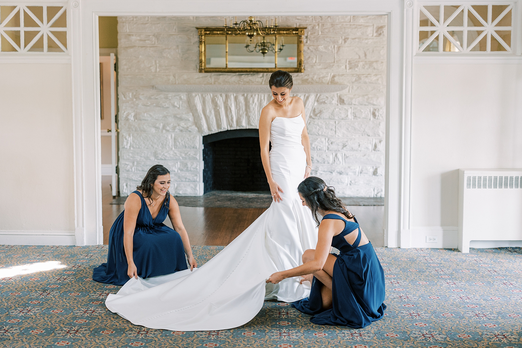 bridesmaids in navy gowns help bride with train of wedding dress